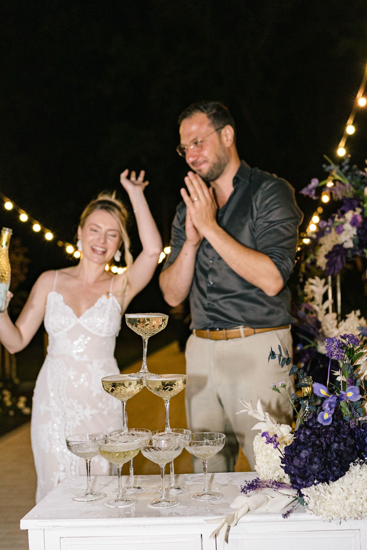 Celebratory champagne tower being filled at an evening wedding reception.