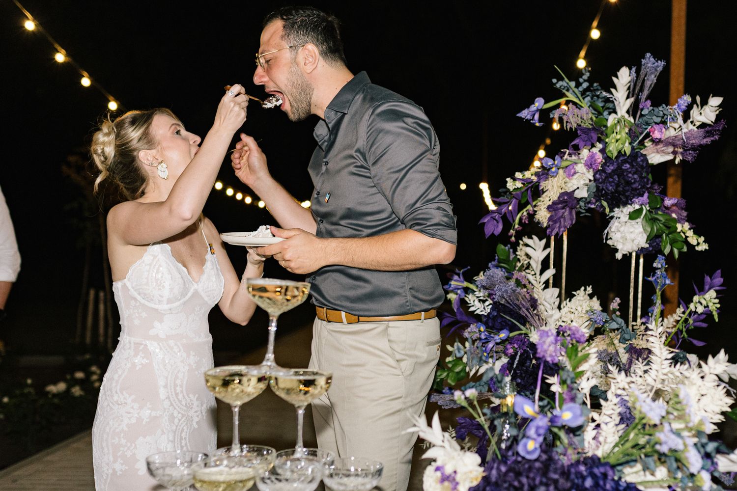 Wedding guests watch as champagne cascades down crystal coupe tower at night.