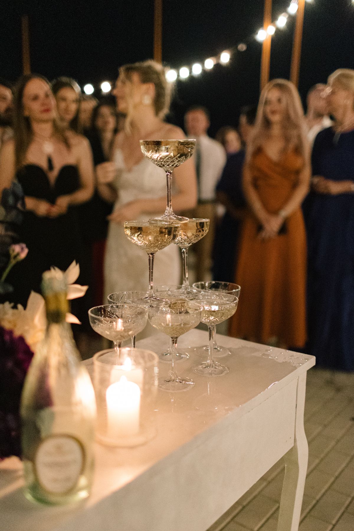 Elegant champagne tower display on white table with candlelight at evening reception.