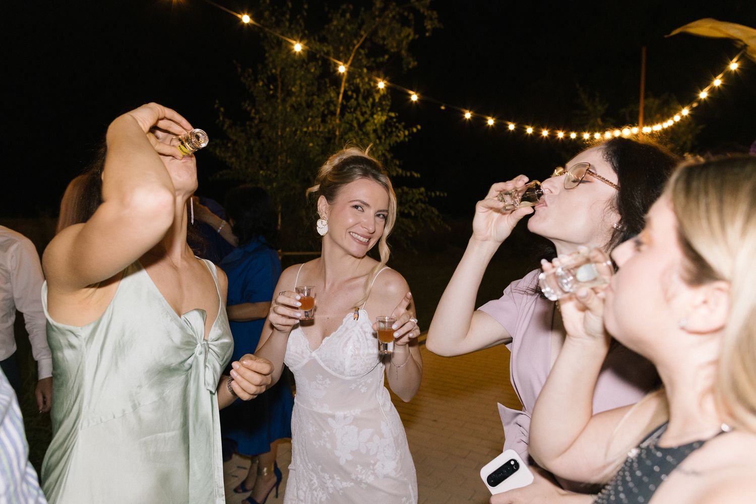 Wedding party taking celebratory shots at nighttime outdoor reception.