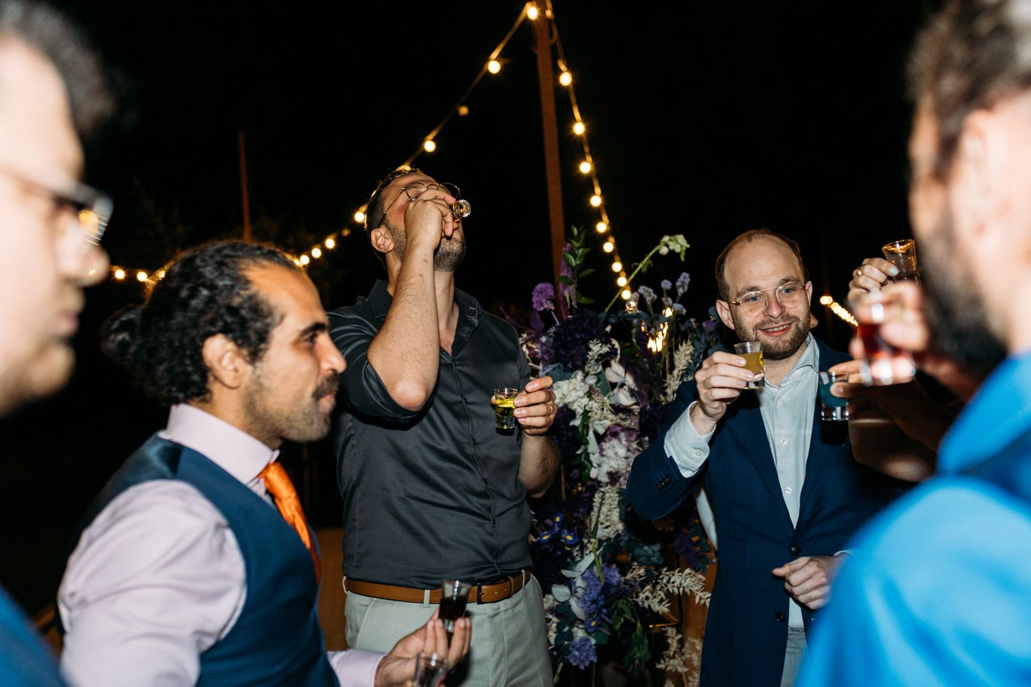 Wedding guests celebrating at outdoor reception with string lights overhead.