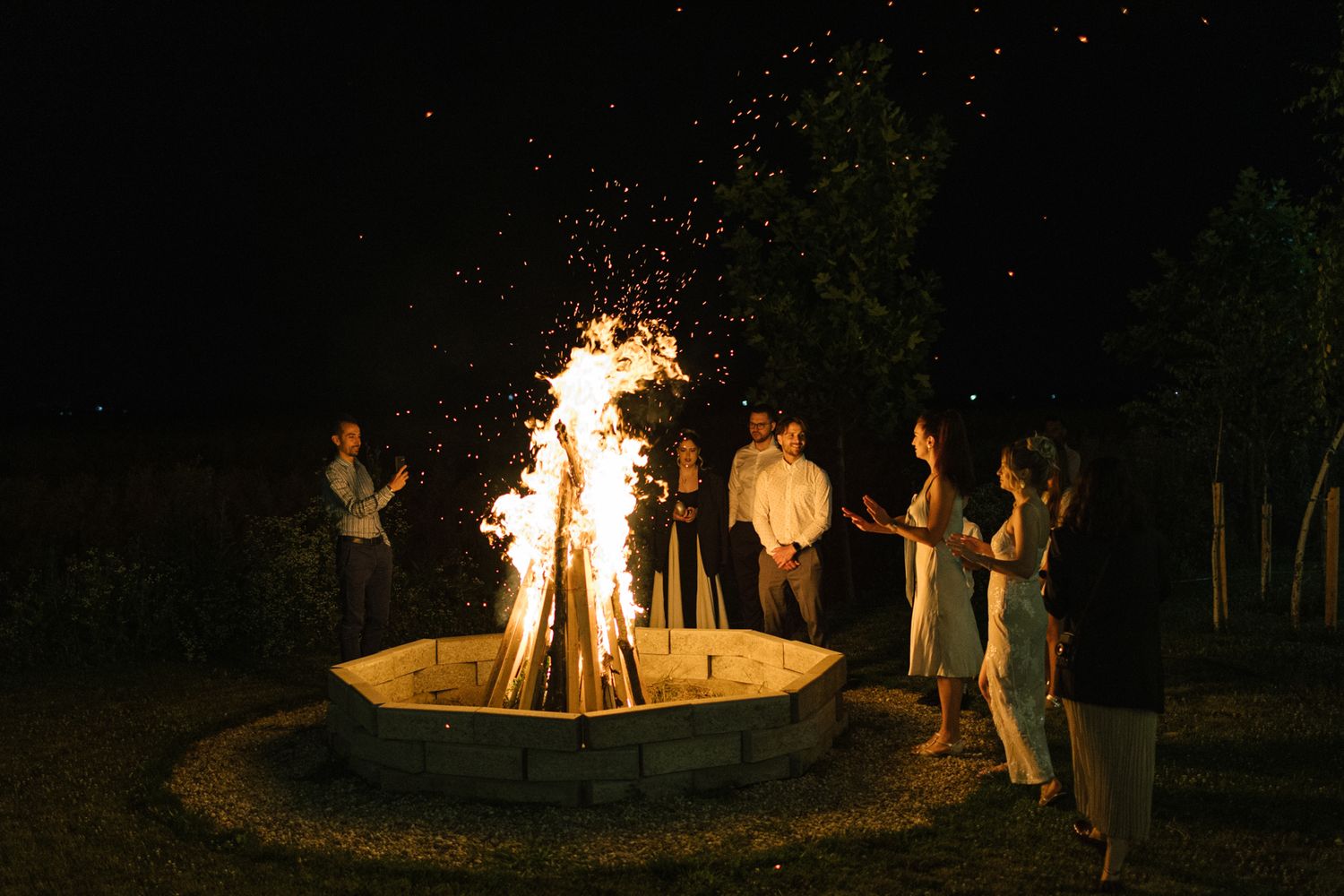 Sparklers illuminate wedding celebration guests gathered in circle at night.