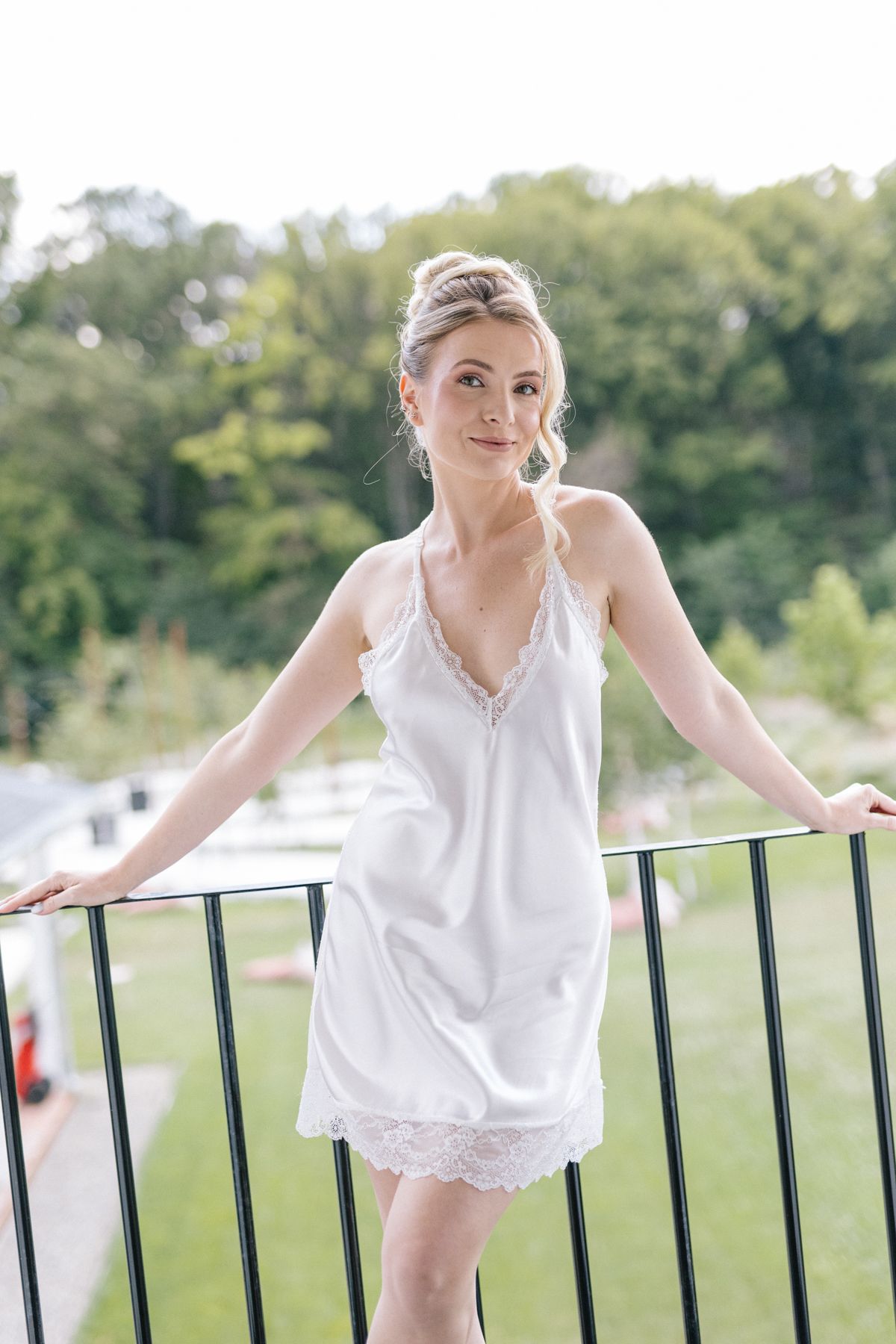 Person in white lace top leaning against outdoor railing in natural setting.
