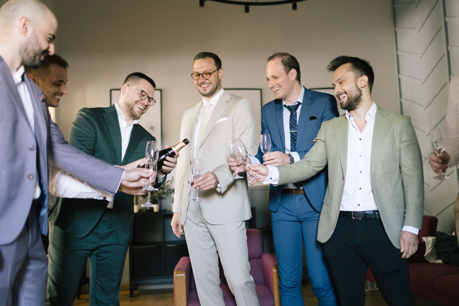 Wedding party members in suits socializing before ceremony in contemporary space.