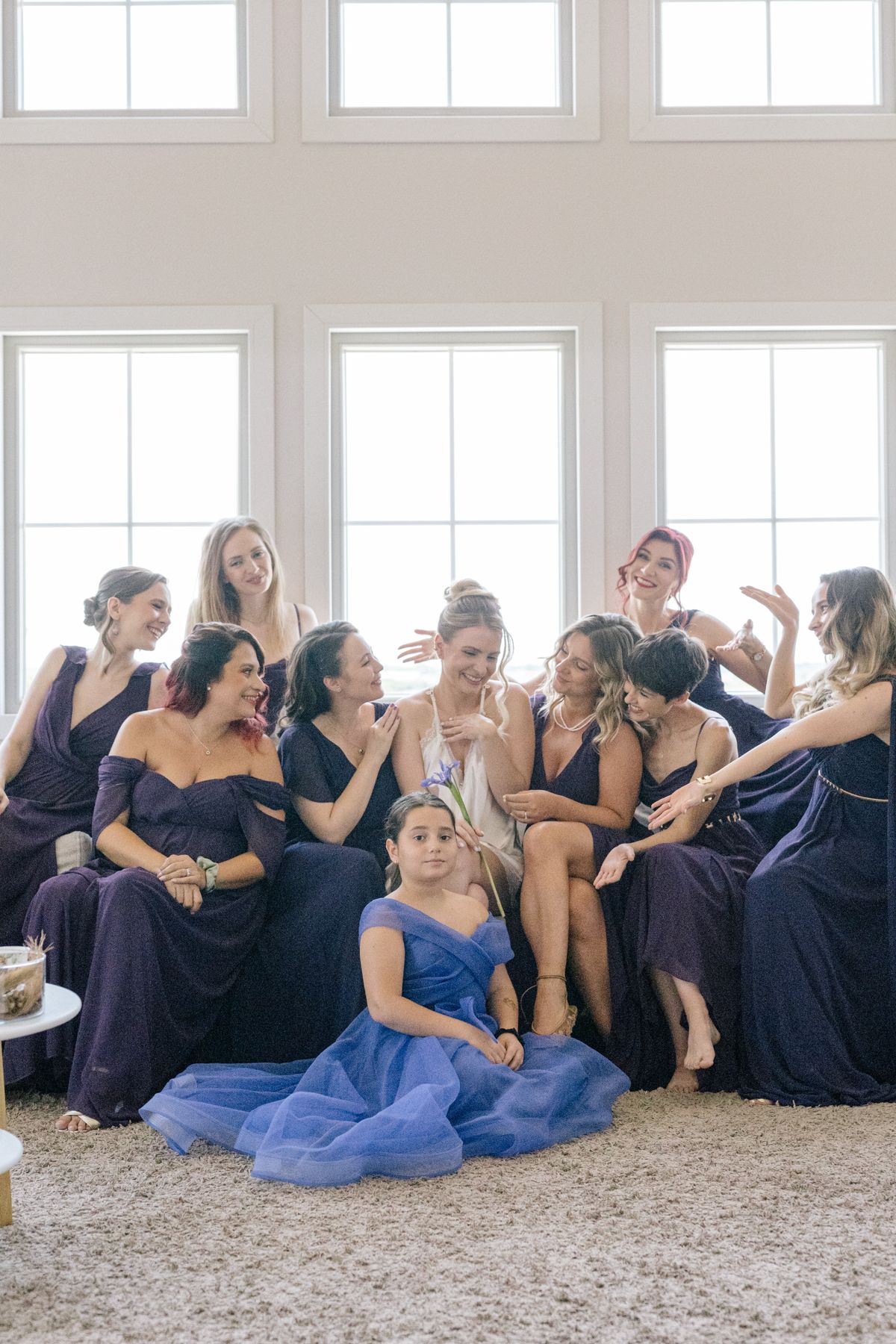 Bridesmaids in purple and blue dresses sharing candid laughs on the floor.