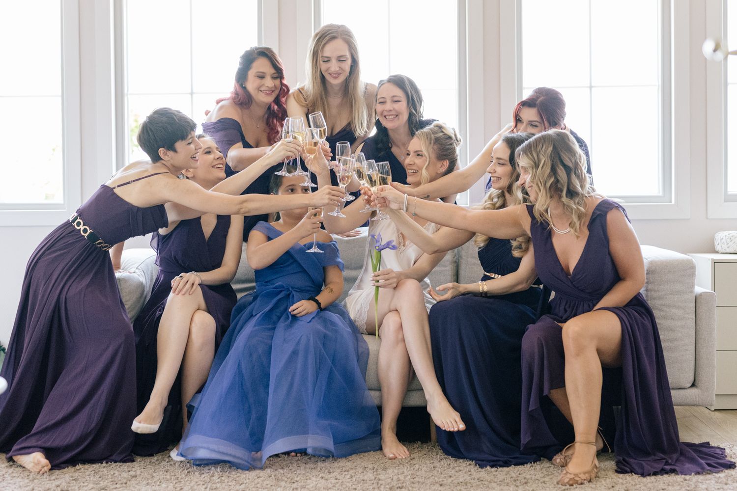 Wedding party bridesmaids in purple dresses posing together on floor.