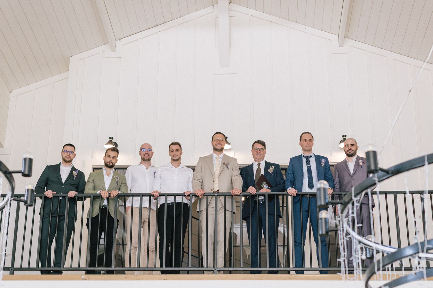 Wedding party in formal attire poses on white balcony railing.