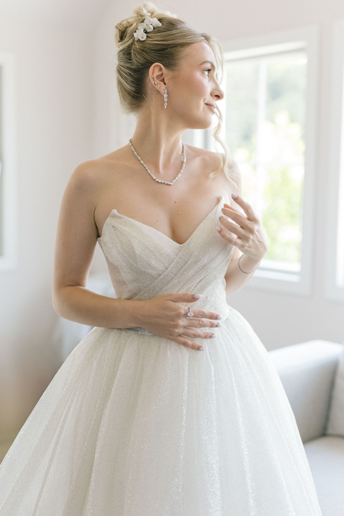 Side profile of bride in strapless ballgown wearing elegant necklace and earrings.