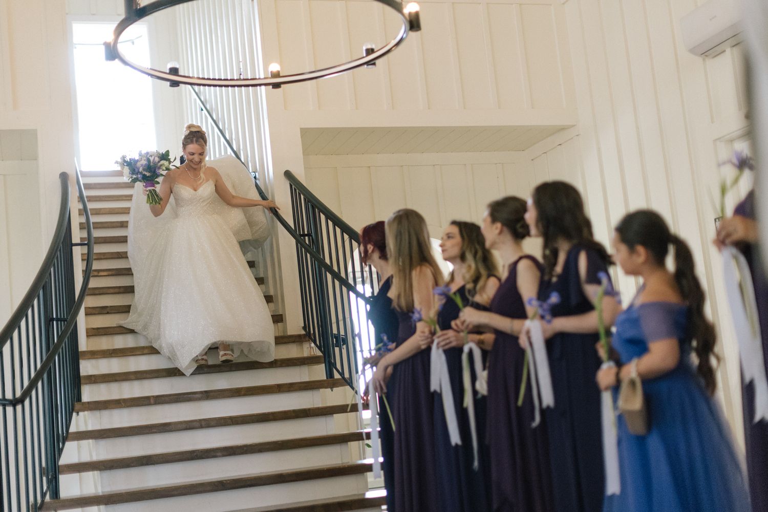 Wedding guests in navy dresses stand along a staircase during a ceremony.