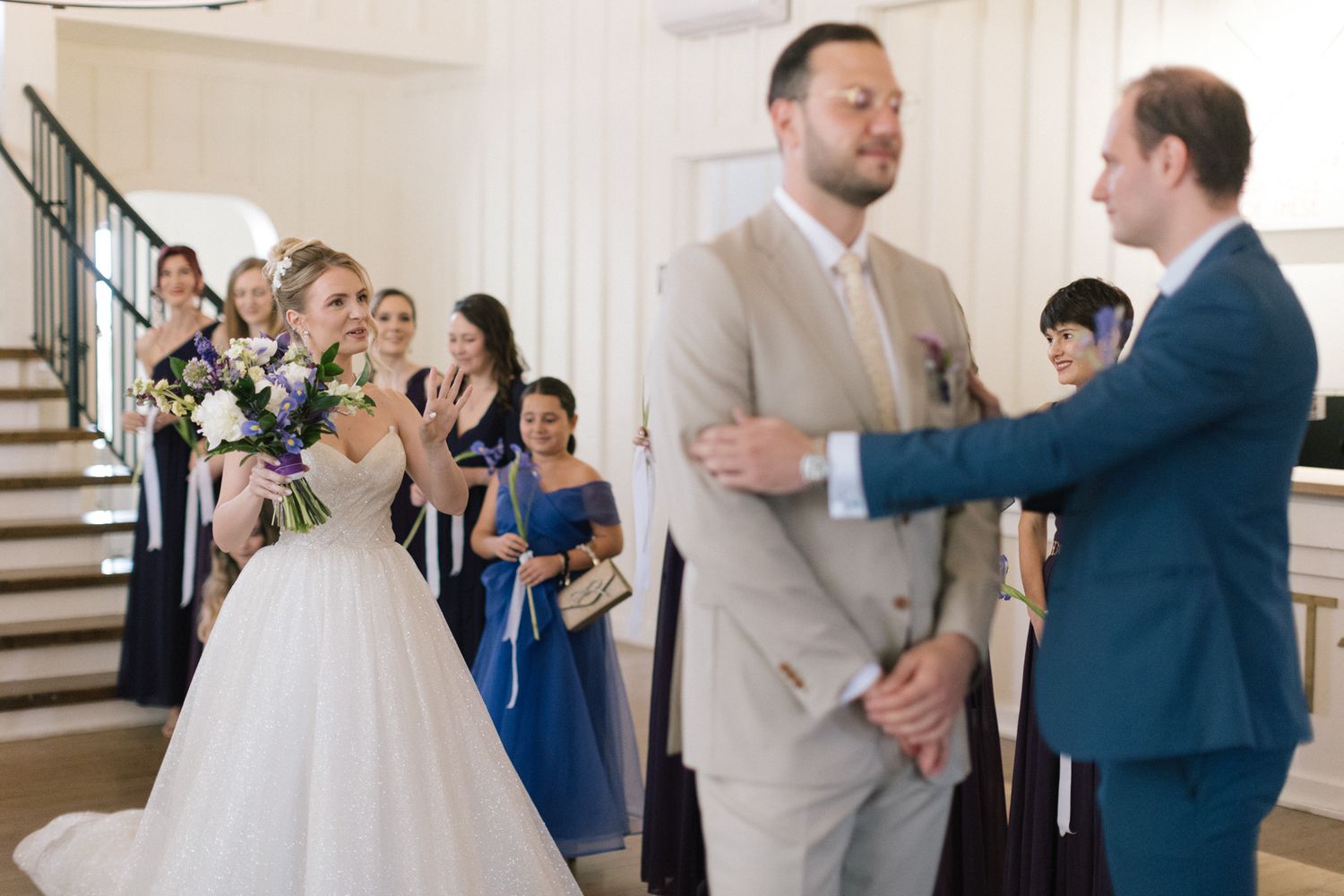 Wedding party members interact during a reception in a bright white venue with elegant decor.