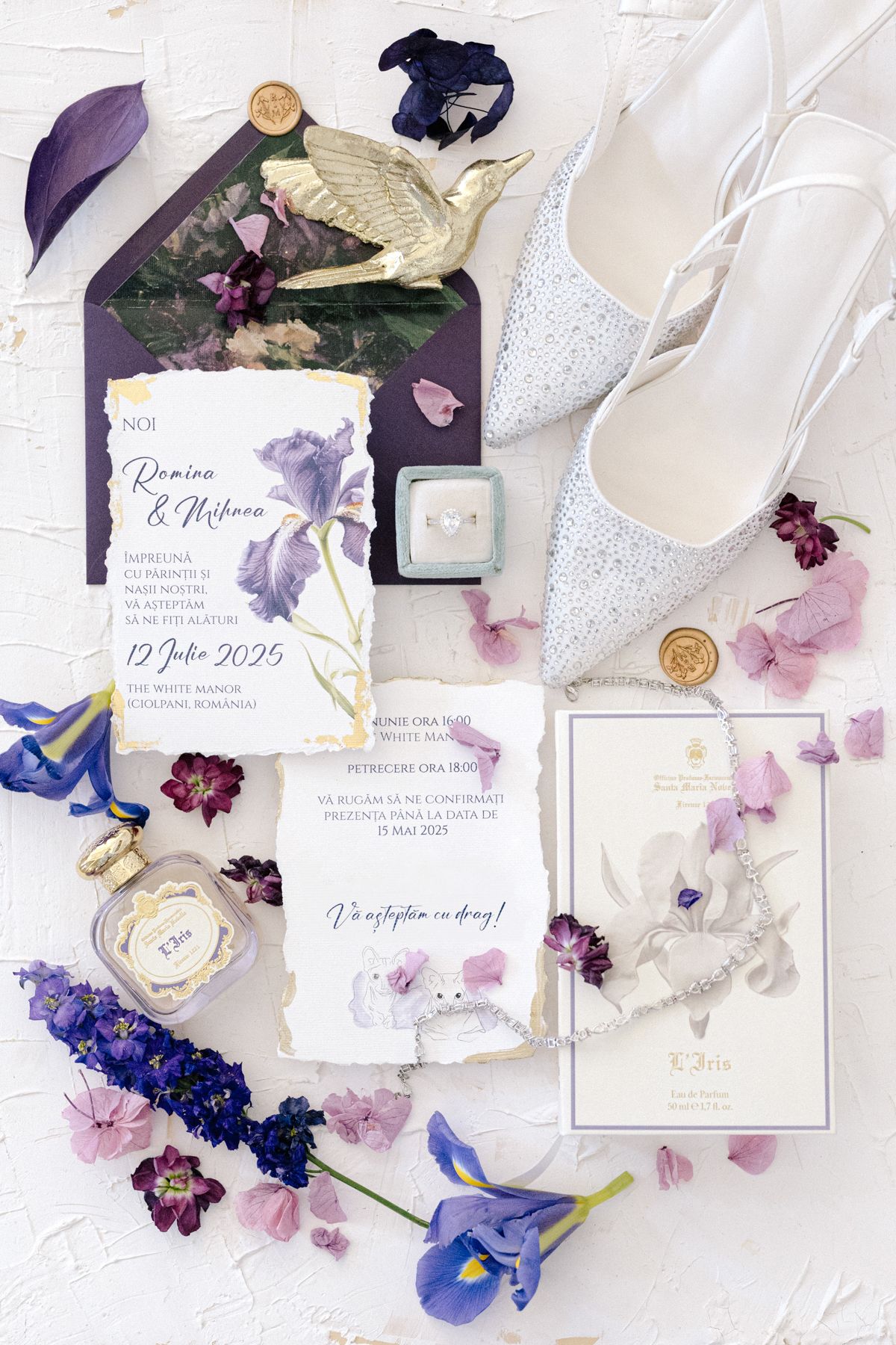 Artistic flat lay of wedding stationery with purple flowers and white lace details.