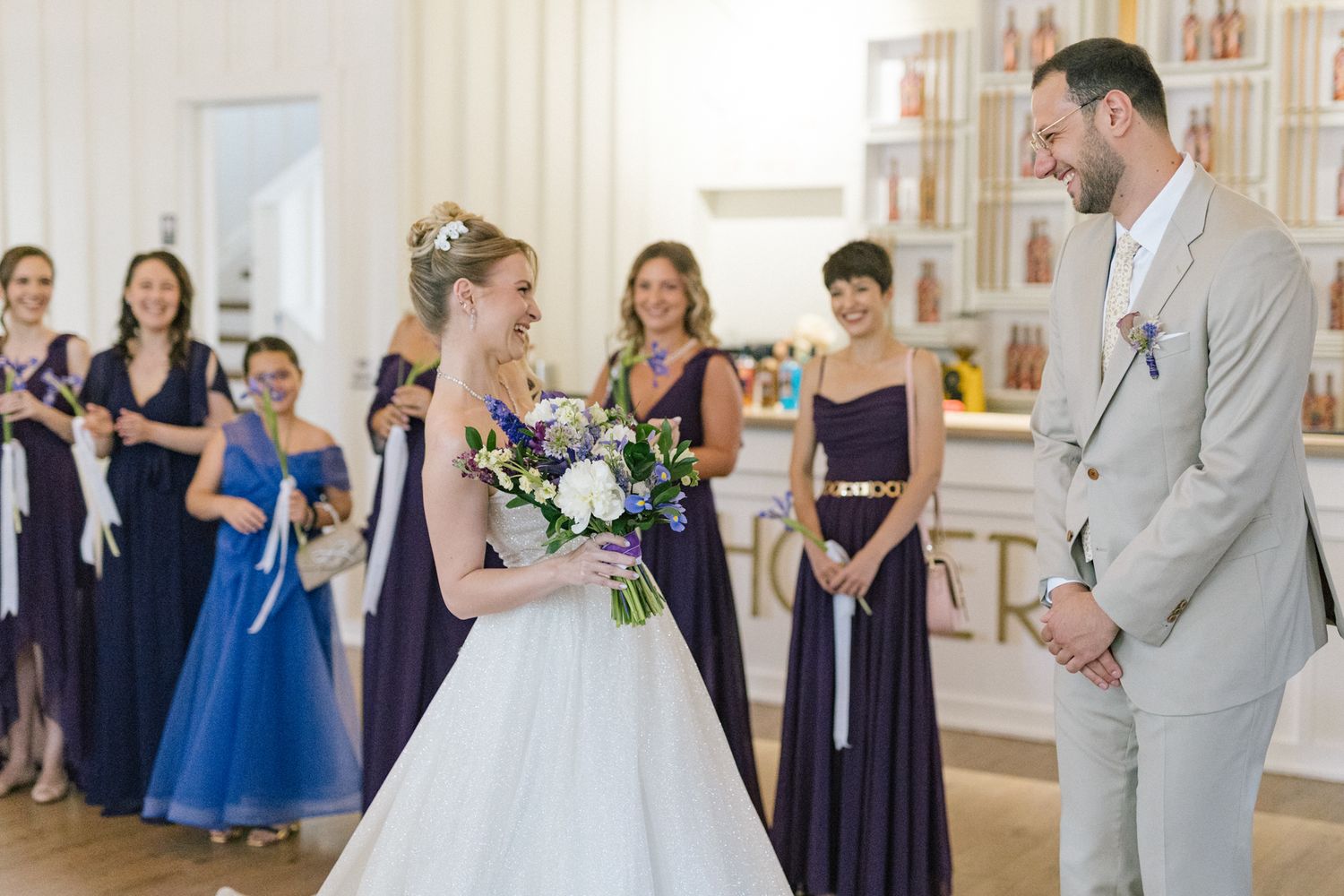 Wedding party members celebrate in an elegant white venue with decorative wall frames.