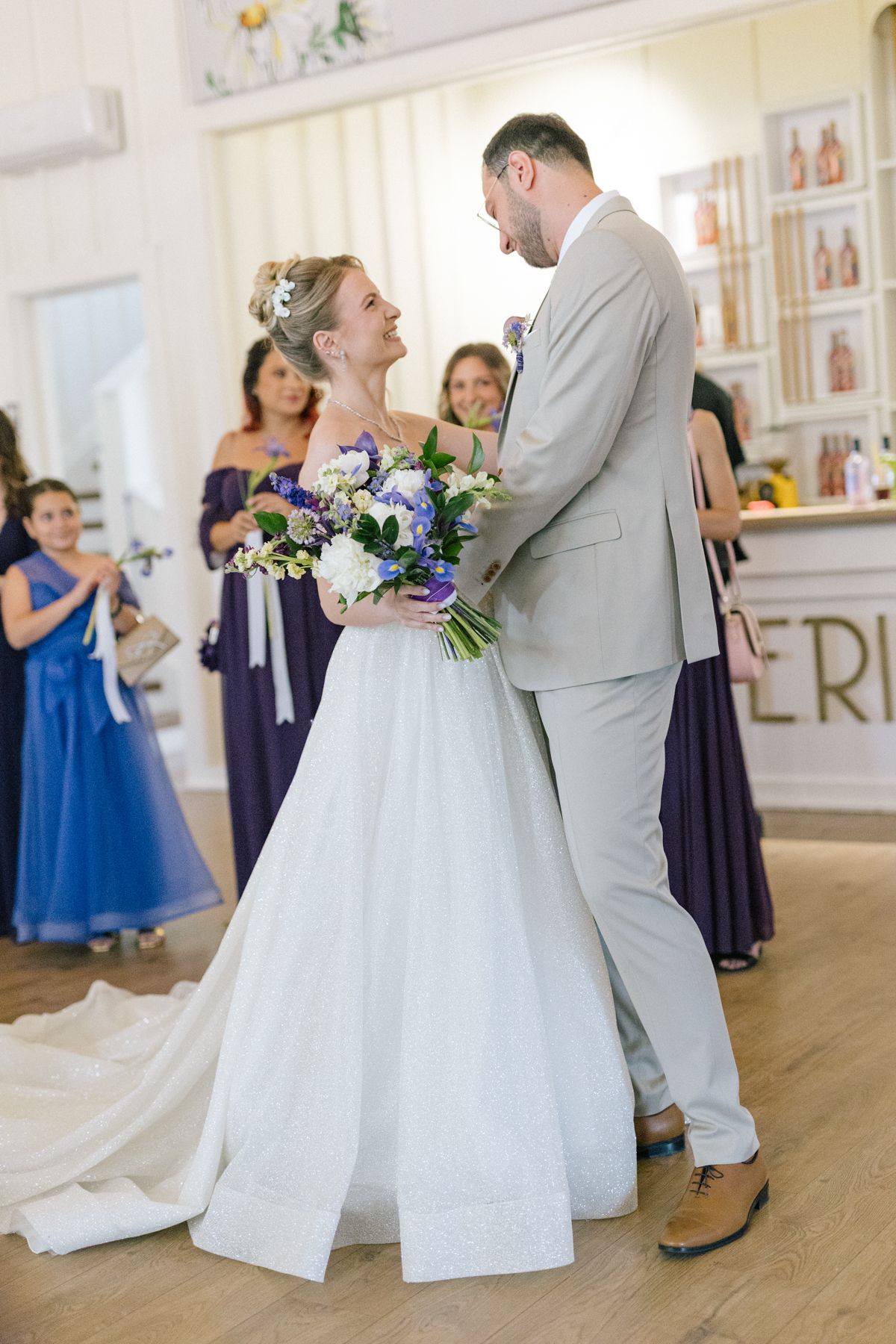 Wedding couple shares their first dance while guests in navy dresses look on.