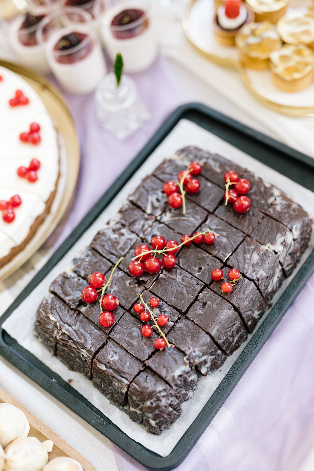 Chocolate brownies decorated with red currants on dark serving plates at wedding dessert table.