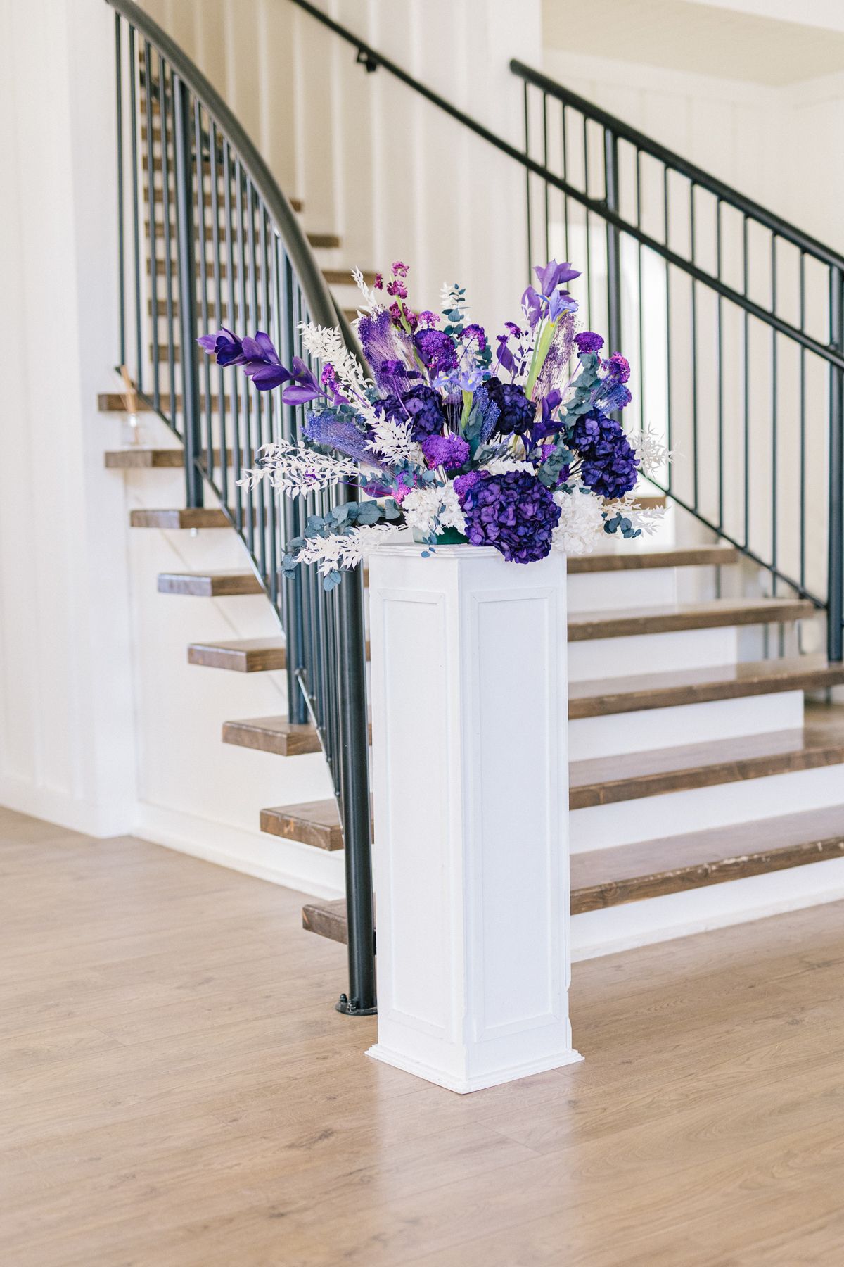 Modern white staircase with wooden steps decorated with purple floral arrangements.