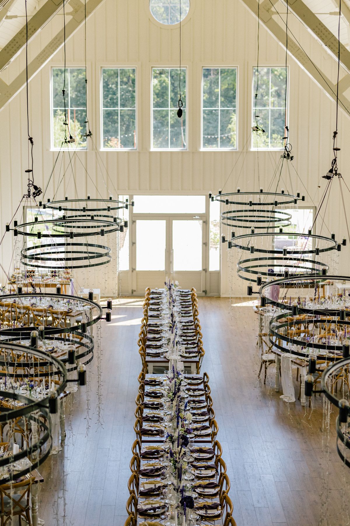 An elegant wedding reception hall with circular chandeliers and rows of wooden chairs.