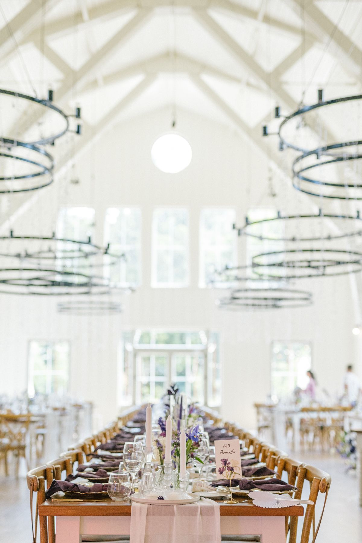 A beautifully set wedding reception table under circular chandeliers in a bright white venue.