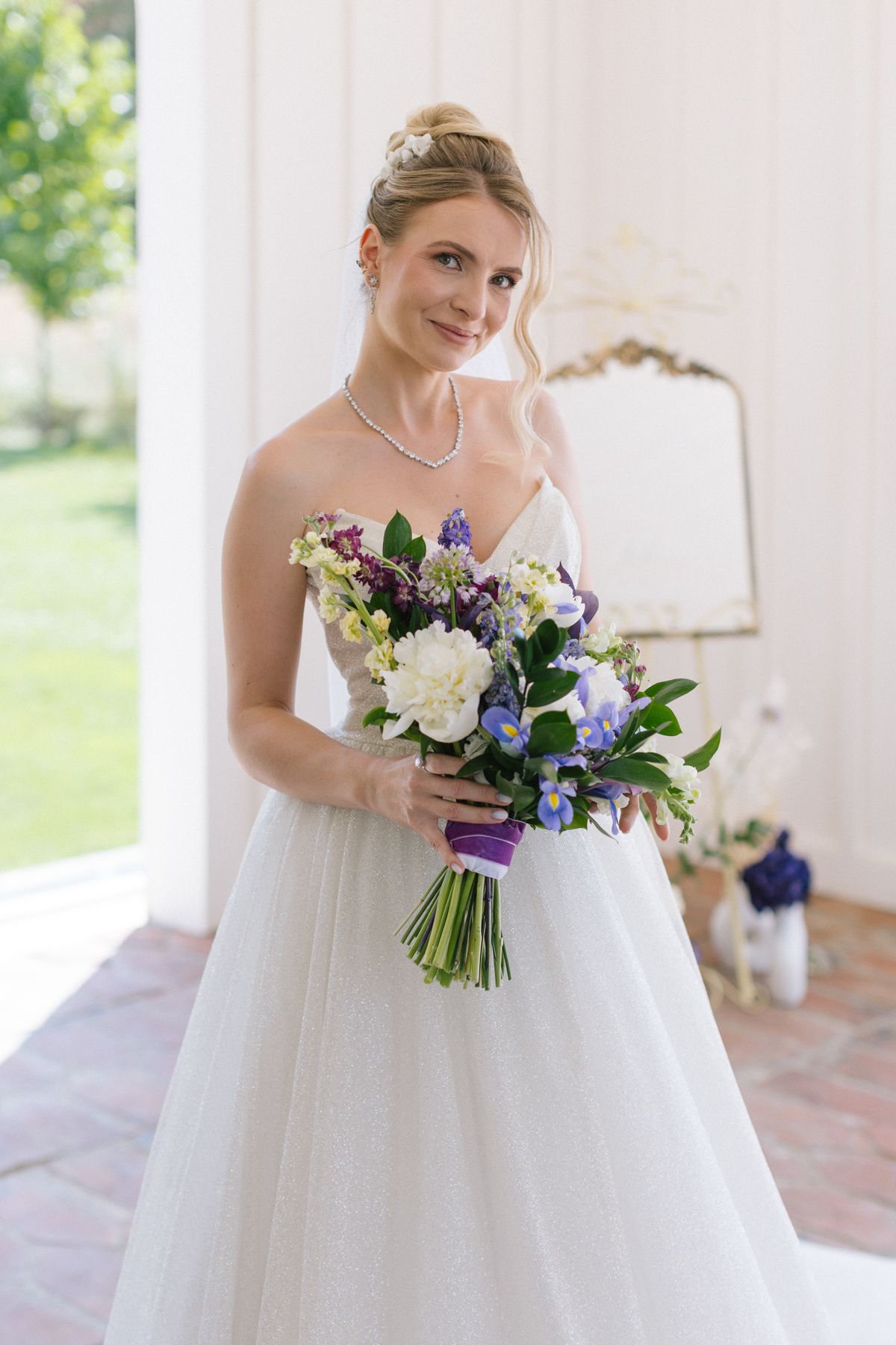 A bride in a strapless white gown holding a purple and white bouquet.