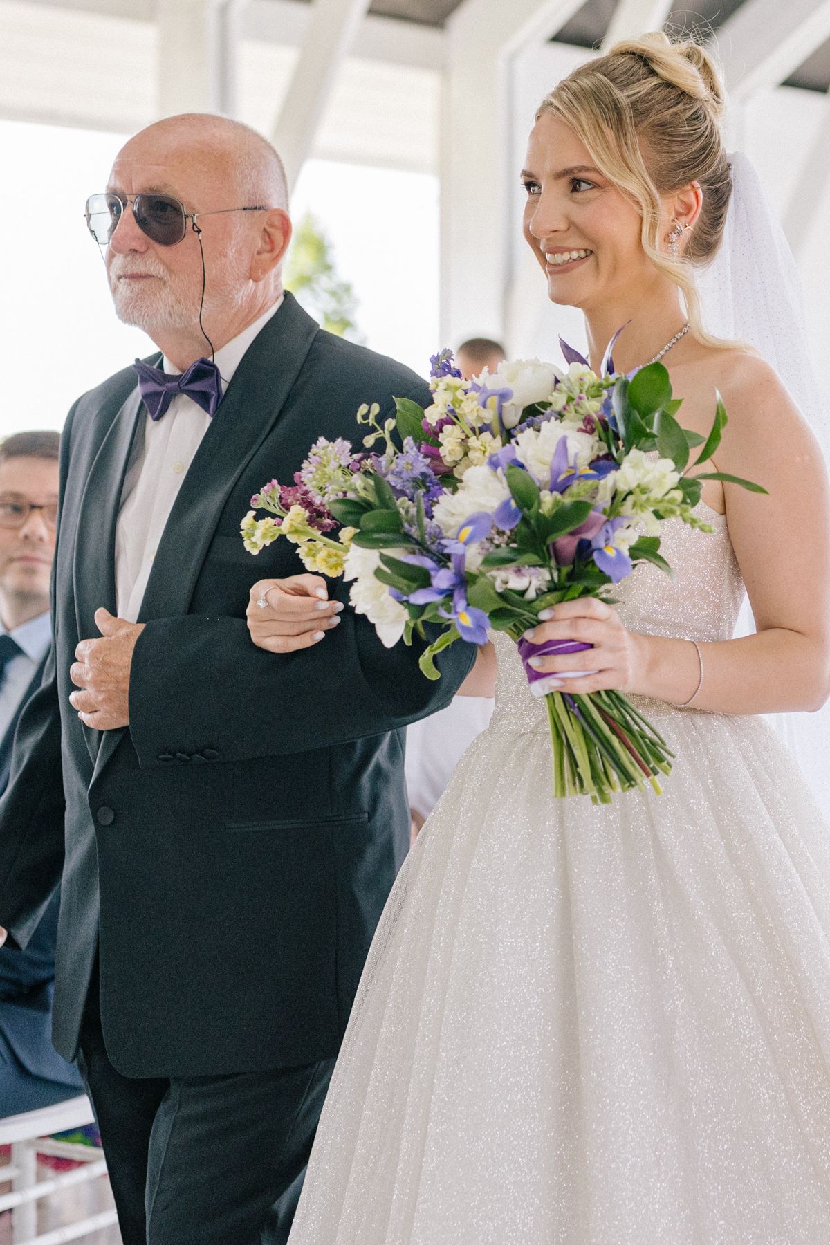 A bride holds a colorful bouquet of purple and white flowers during the ceremony.