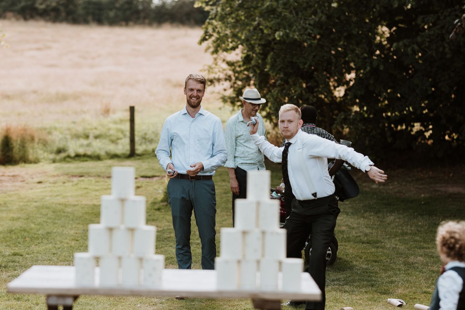 Wedding guests play a giant outdoor can throw game during a backyard reception celebration.