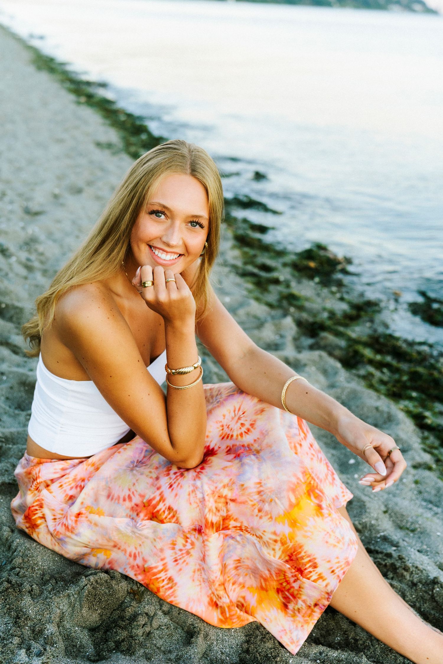 Person in white top and coral tie-dye skirt poses on beach at sunset in series of casual portraits.