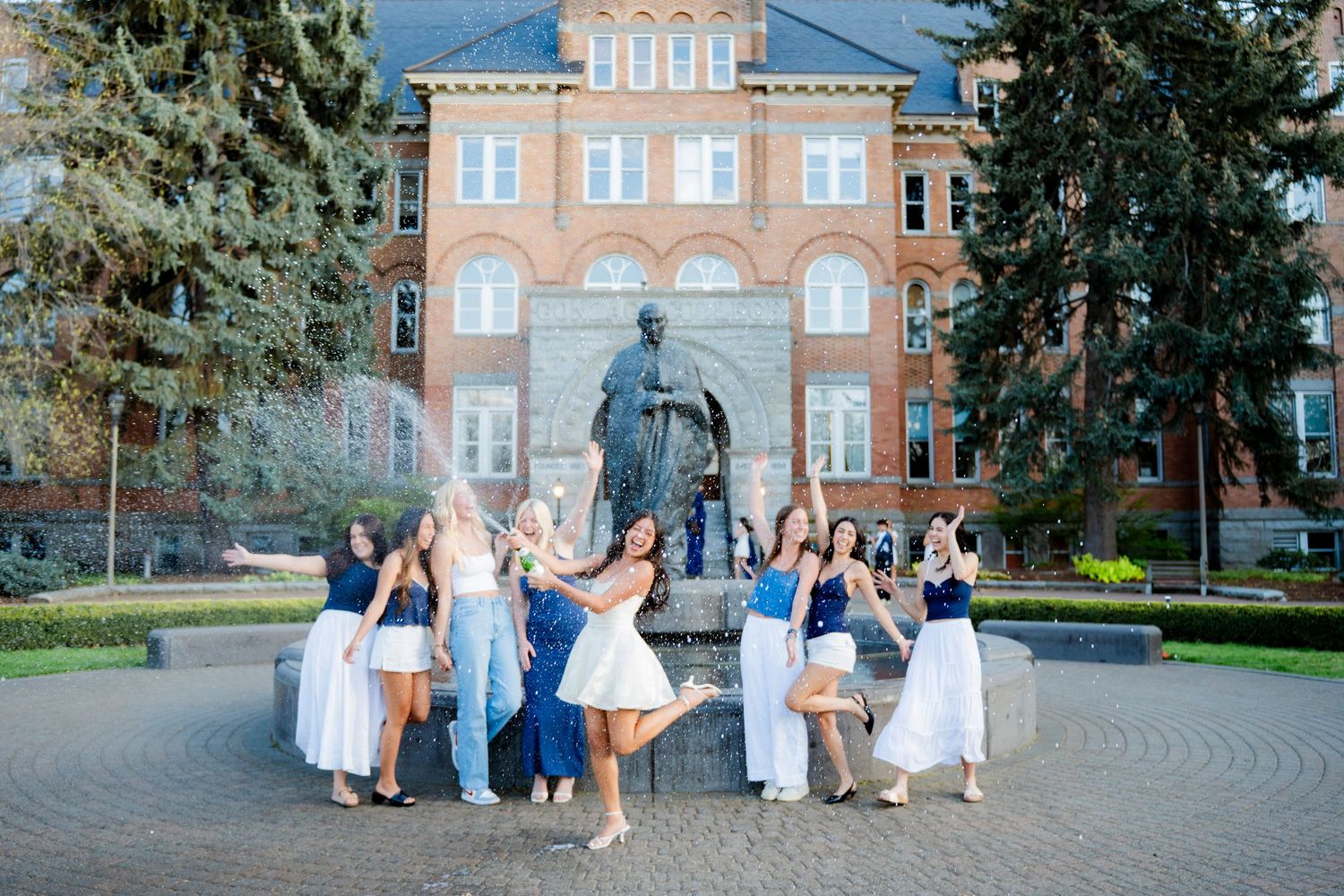 Wedding party poses together in front of a historic brick mansion on a sunny autumn day.