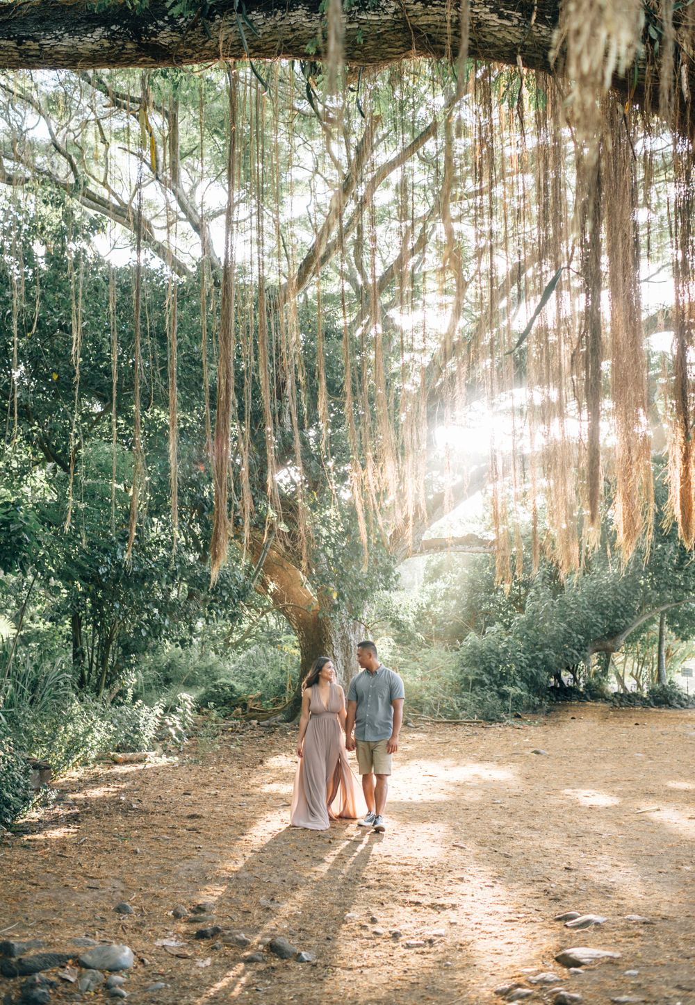 Sunbeams filter through trees as a couple walks along a forest trail.