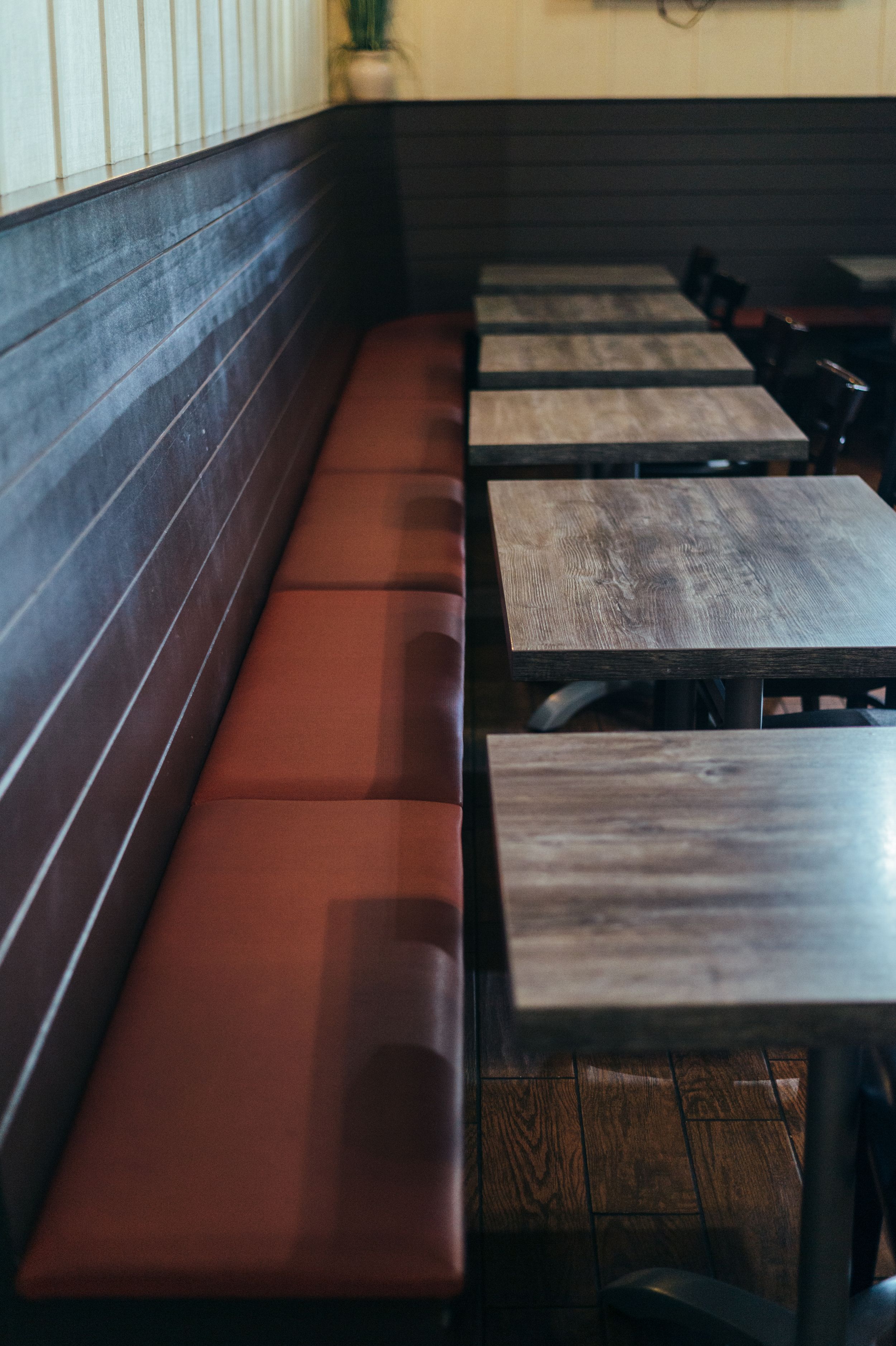 Restaurant interior with red leather bench seating and wooden tables along wall.