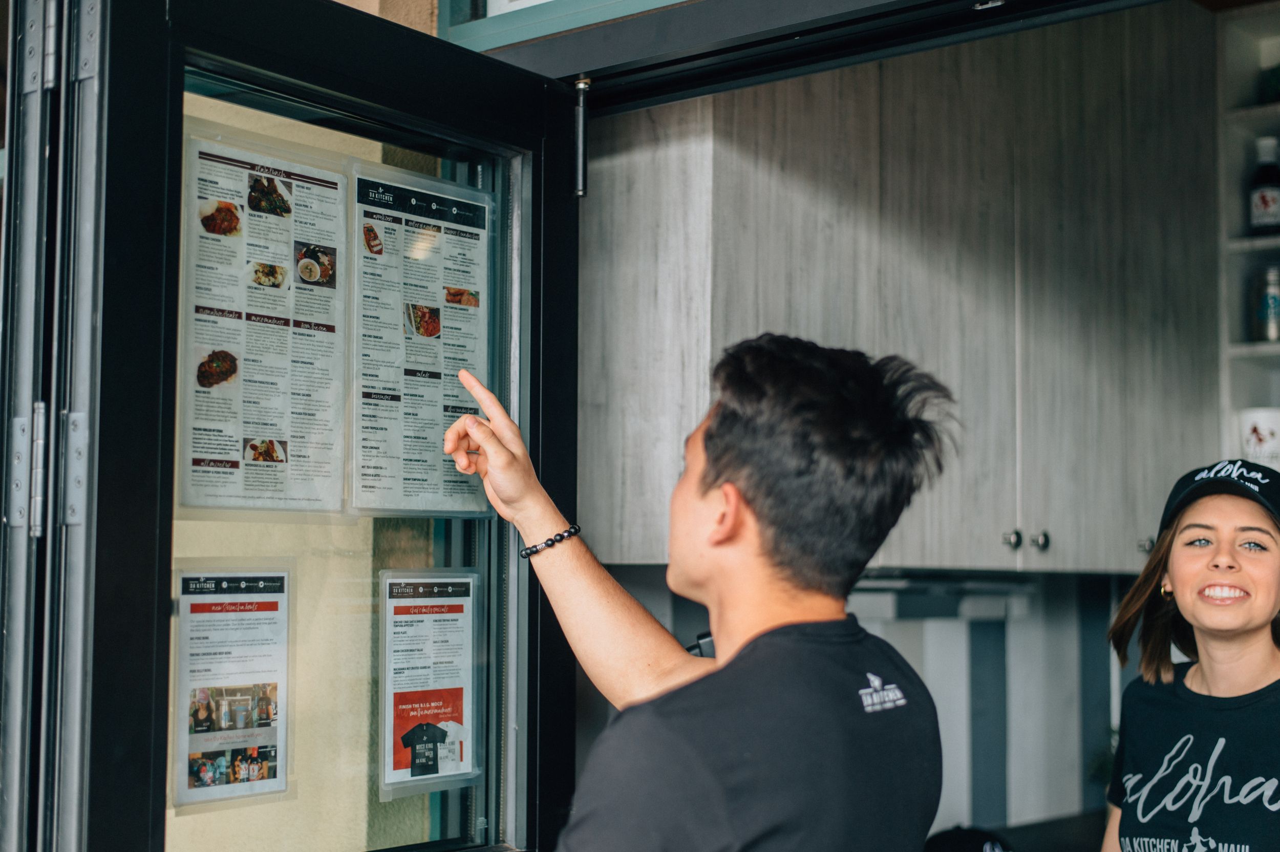 Customer pointing at menu board displaying food options in restaurant interior.
