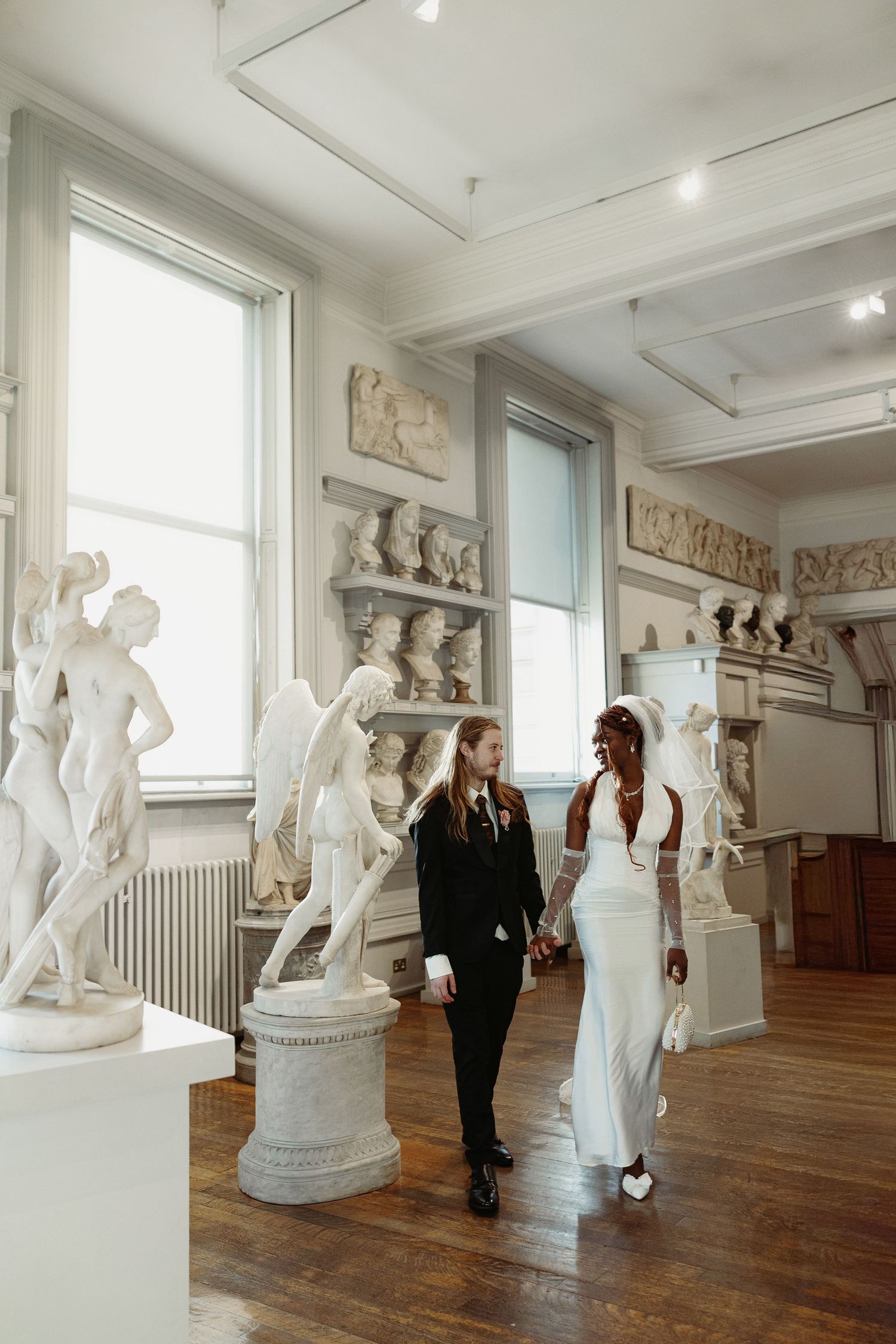 White marble sculptures and statues on display in a museum gallery with wooden floors and natural lighting.