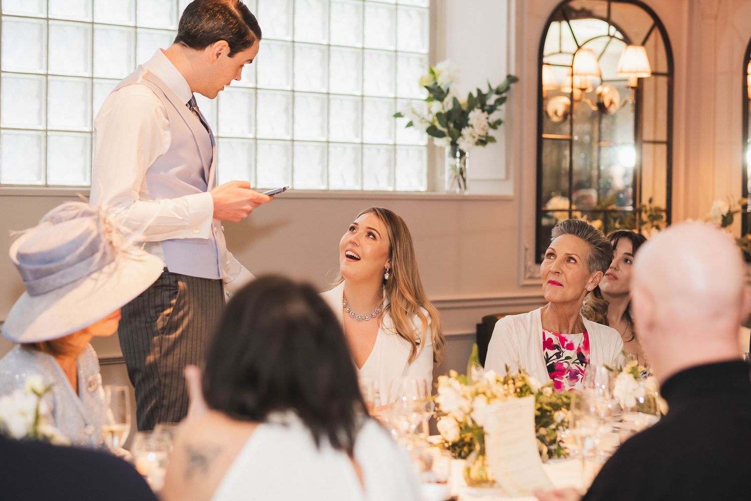 A candid reception scene shows guests seated at tables with elegant floral centerpieces in Bellanger Islington