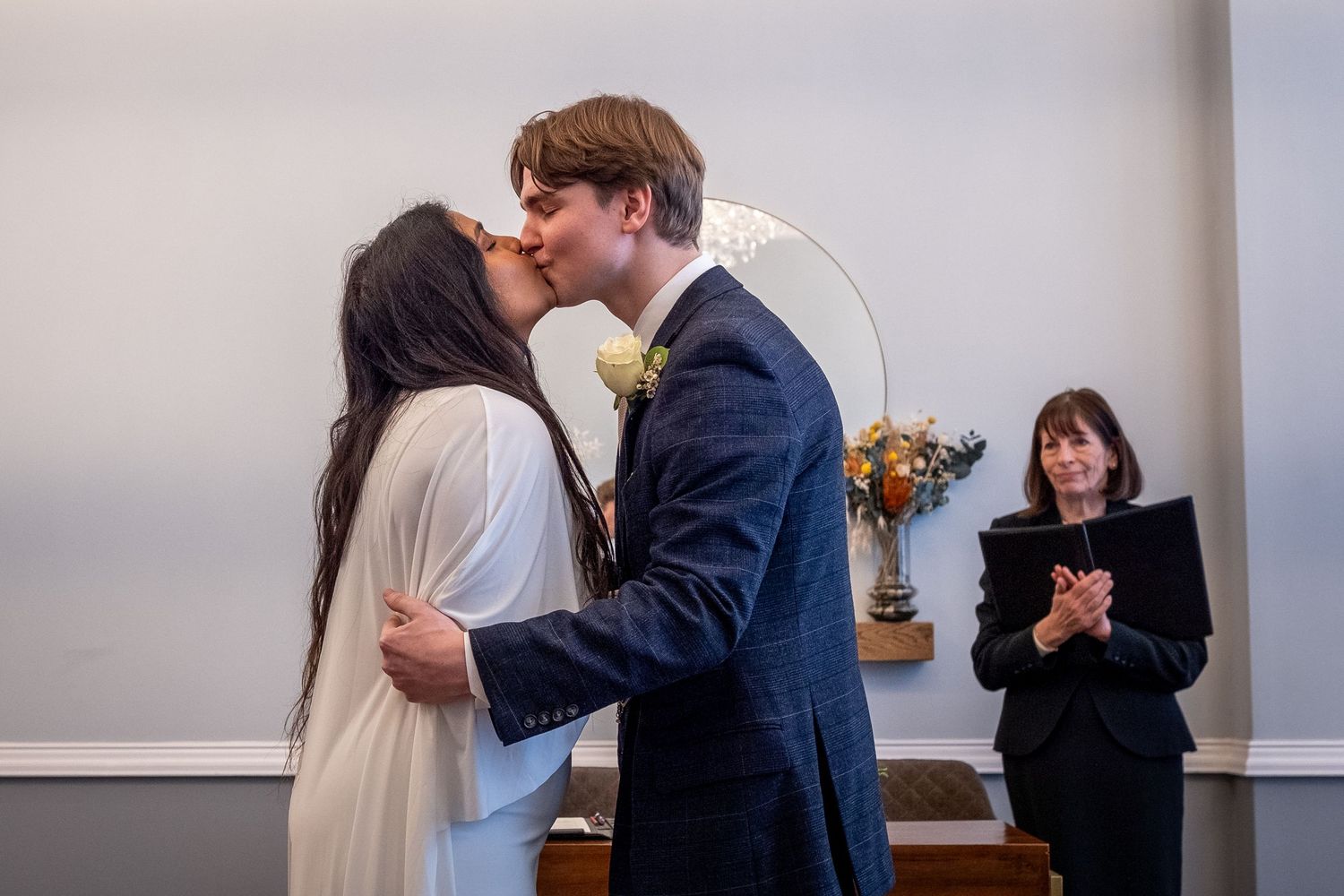 A couple shares a kiss during an intimate wedding ceremony while an officiant stands in the background at Islington Town Hall