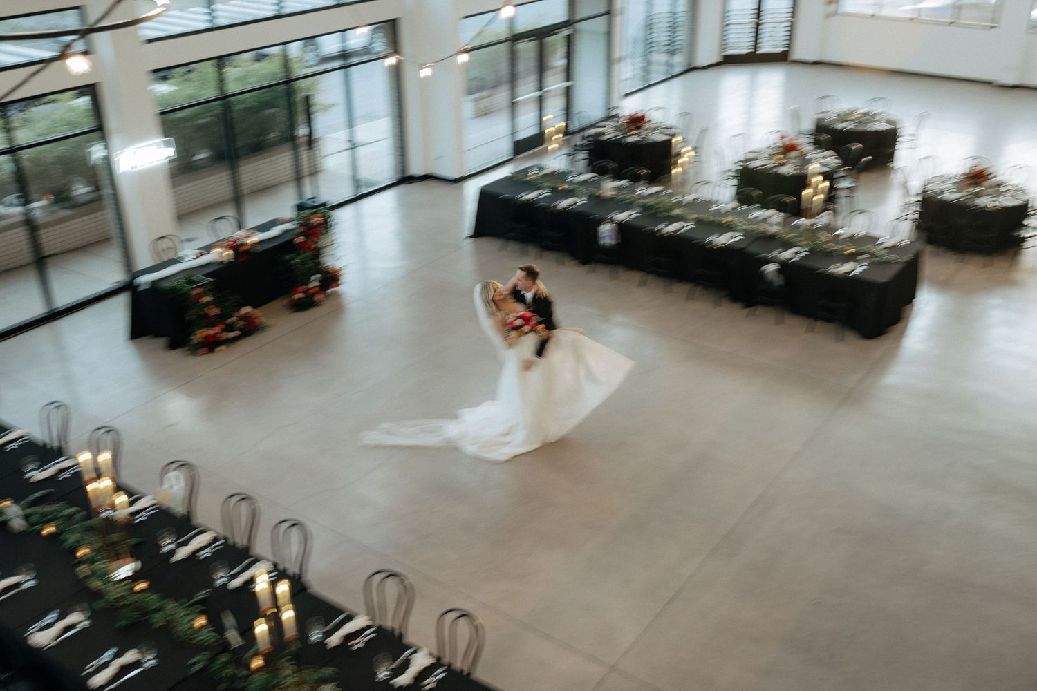 Aerial view of a wedding dress twirling on a modern gray floor with black furniture in a spacious venue.