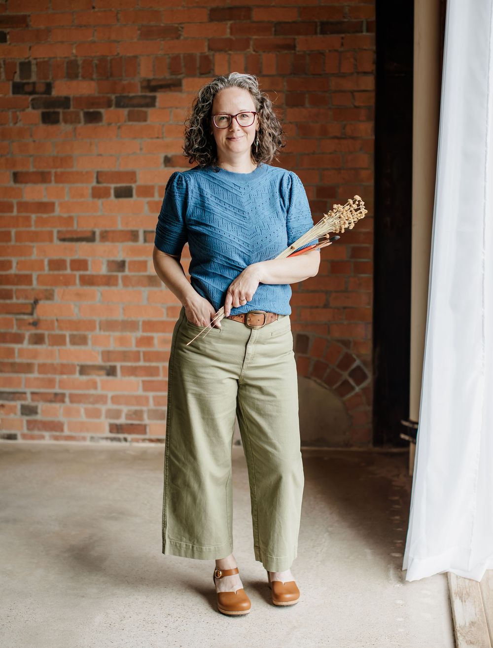 Full-length view of casual outfit with blue sweater and khaki pants against brick wall.