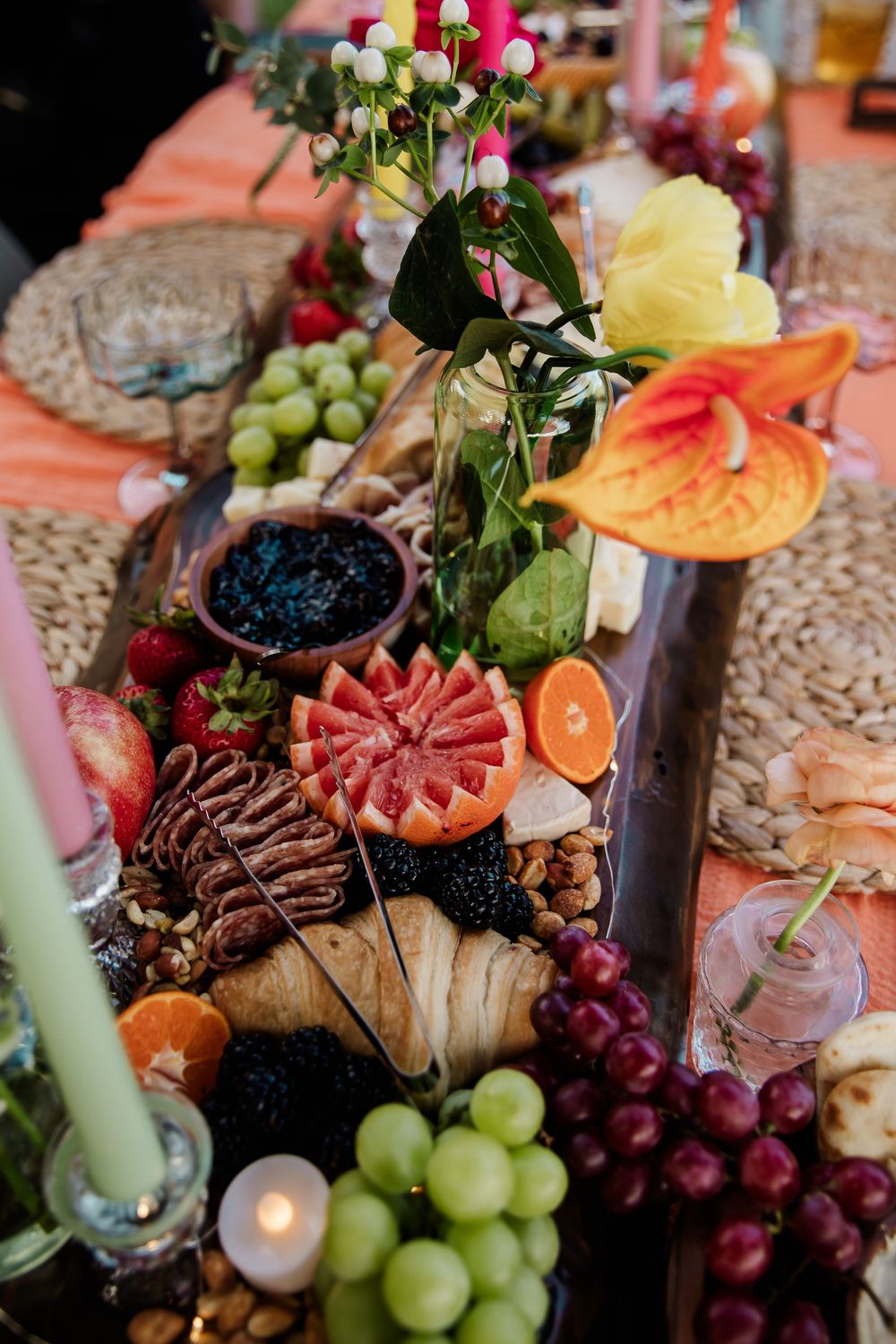 Elaborate charcuterie board with fruits, meats, and colorful garnishes on a decorated table.