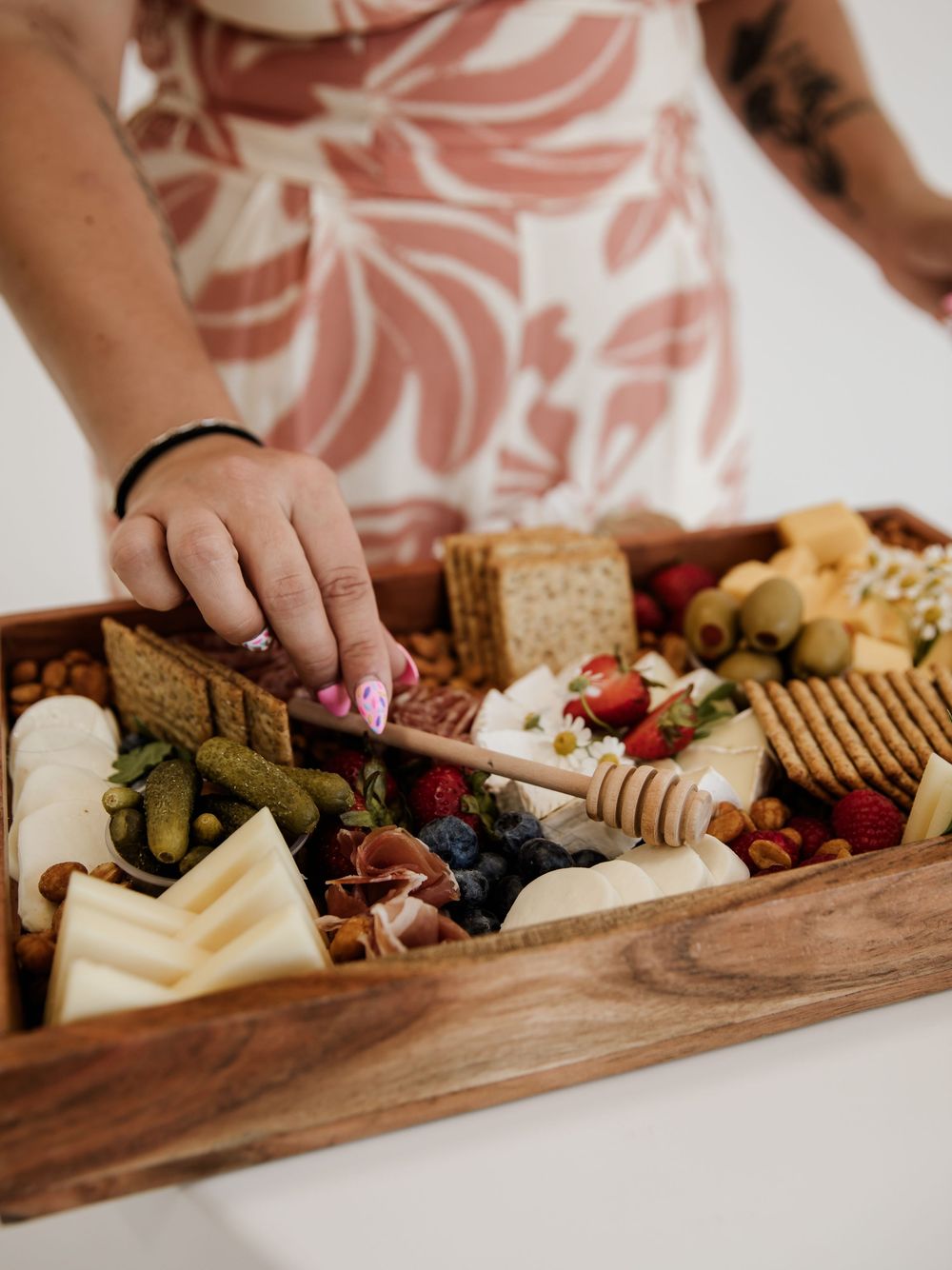 Detailed view of hands arranging food and decorations on a wooden serving board.