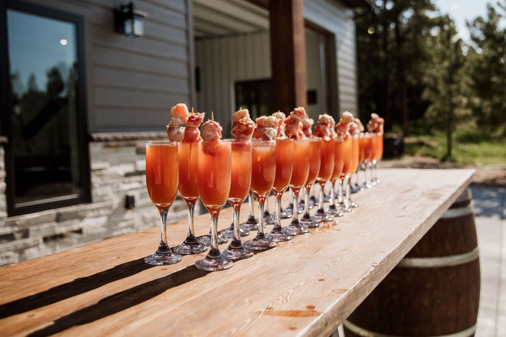 Row of bright orange cocktails lined up on wooden barrels at an outdoor venue.