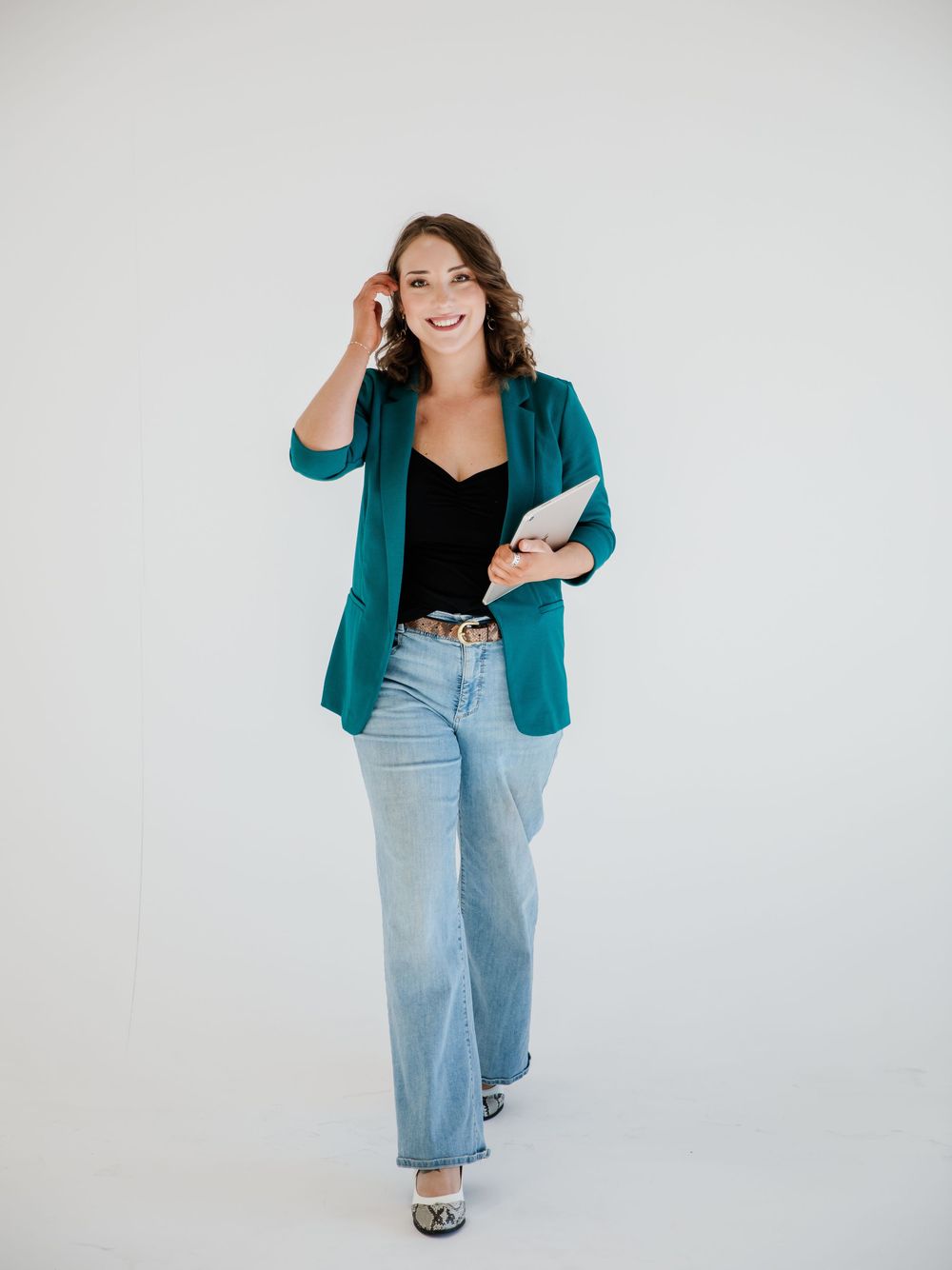 Person in teal blazer and denim poses playfully against white backdrop.