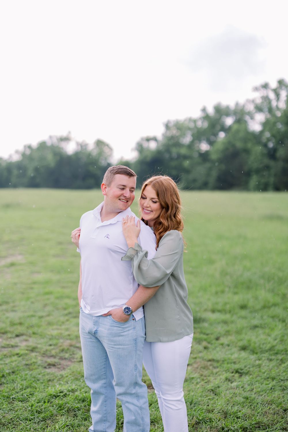 A couple shares a tender moment together while standing in a grassy field on a sunny day.