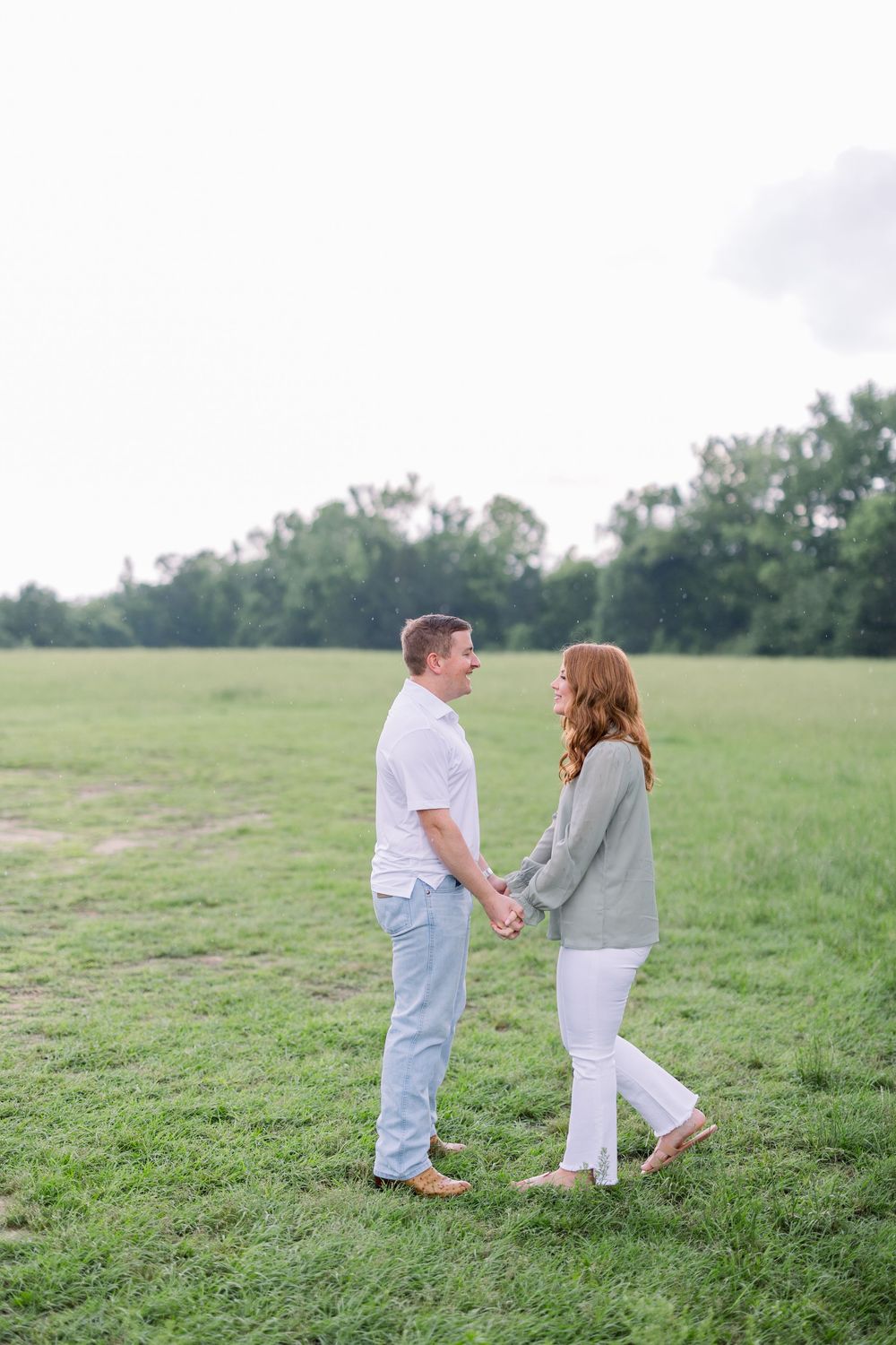 A couple shares a playful moment running and holding hands in a green meadow on a summer day.