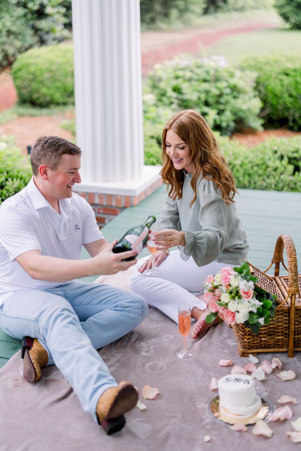 A romantic picnic scene on a porch with champagne, flowers, and a wicker basket.