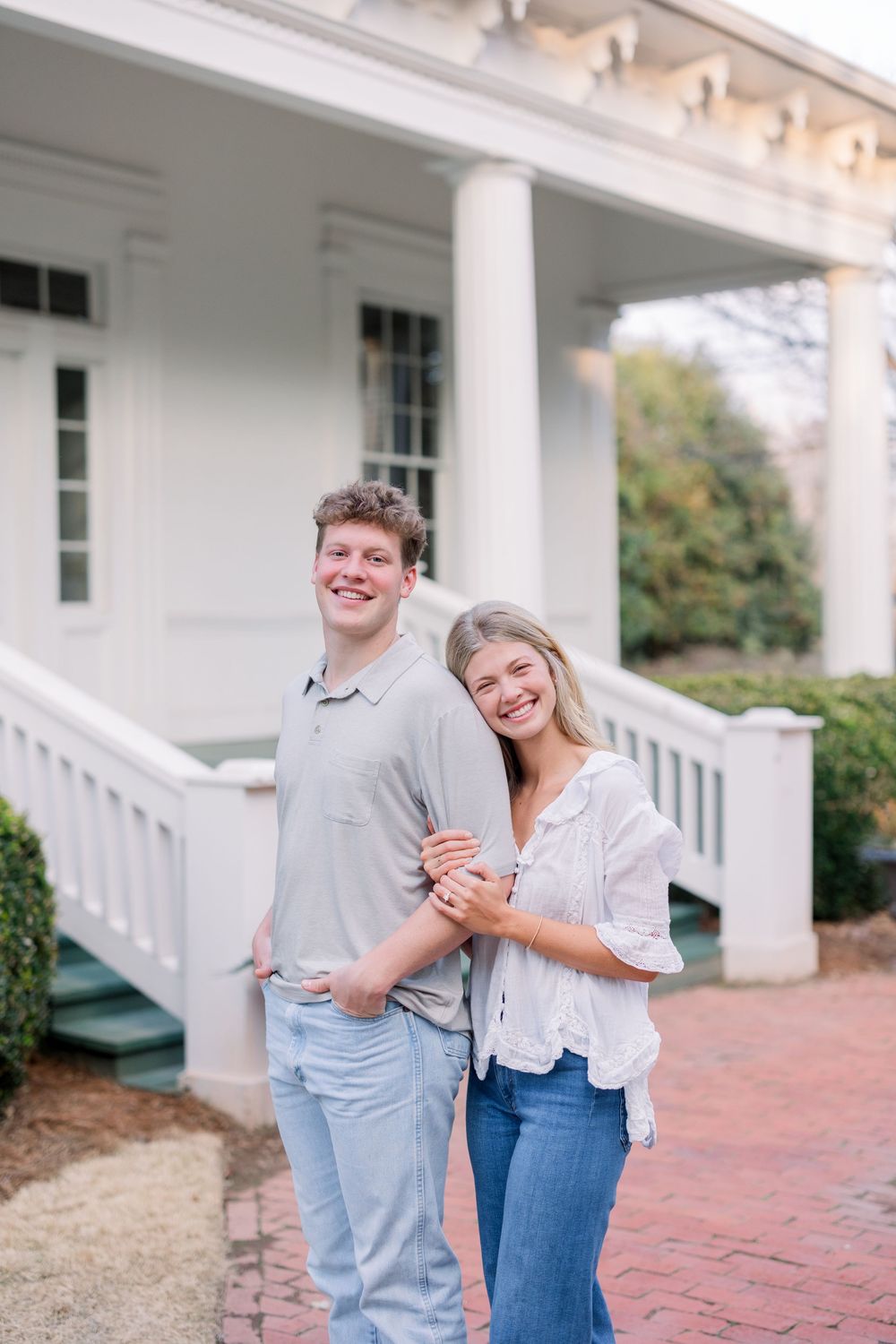 A couple shares playful laughter on a white-columned porch with brick pavers.