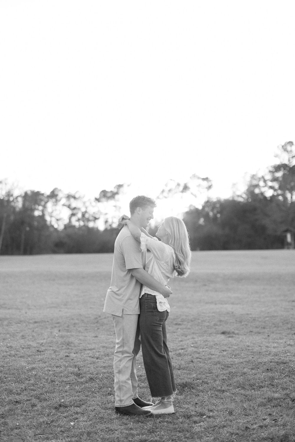 Black and white romantic portraits of a couple embracing in an open field at sunset.