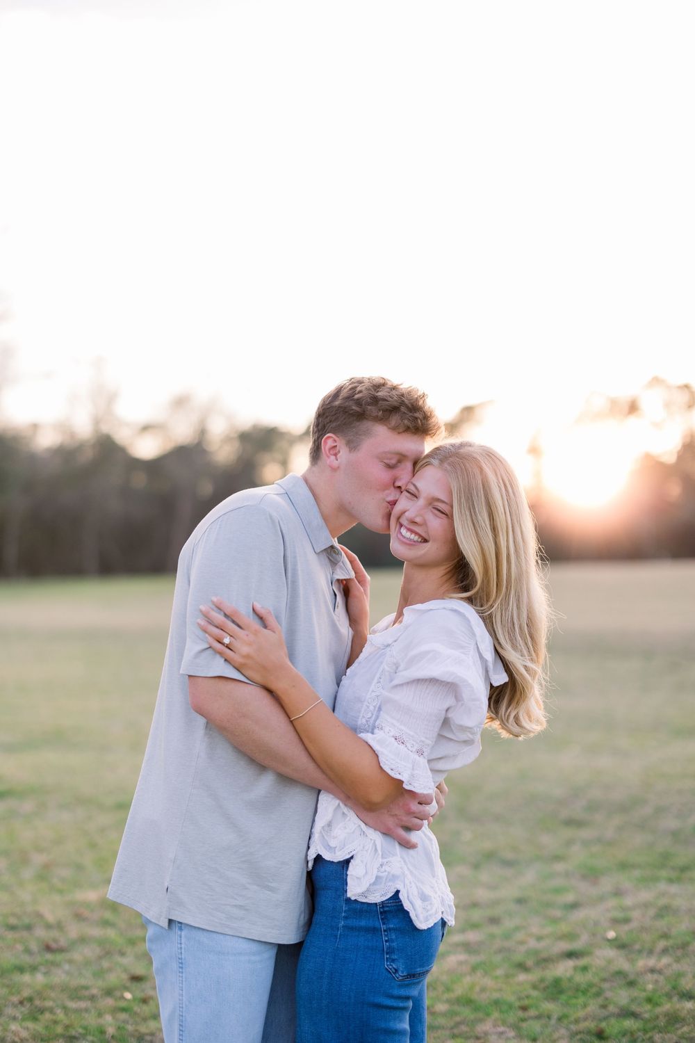 Romantic couple embraces in a sun-drenched field during golden hour photoshoot.
