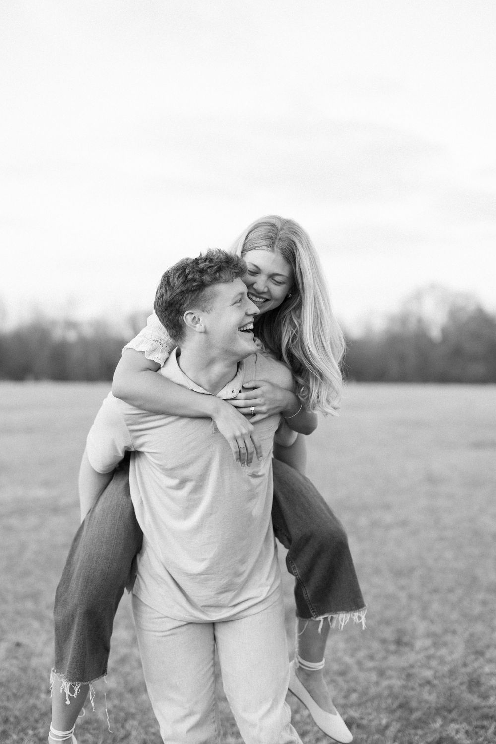 A couple embraces playfully in a sunlit field during their engagement photoshoot.