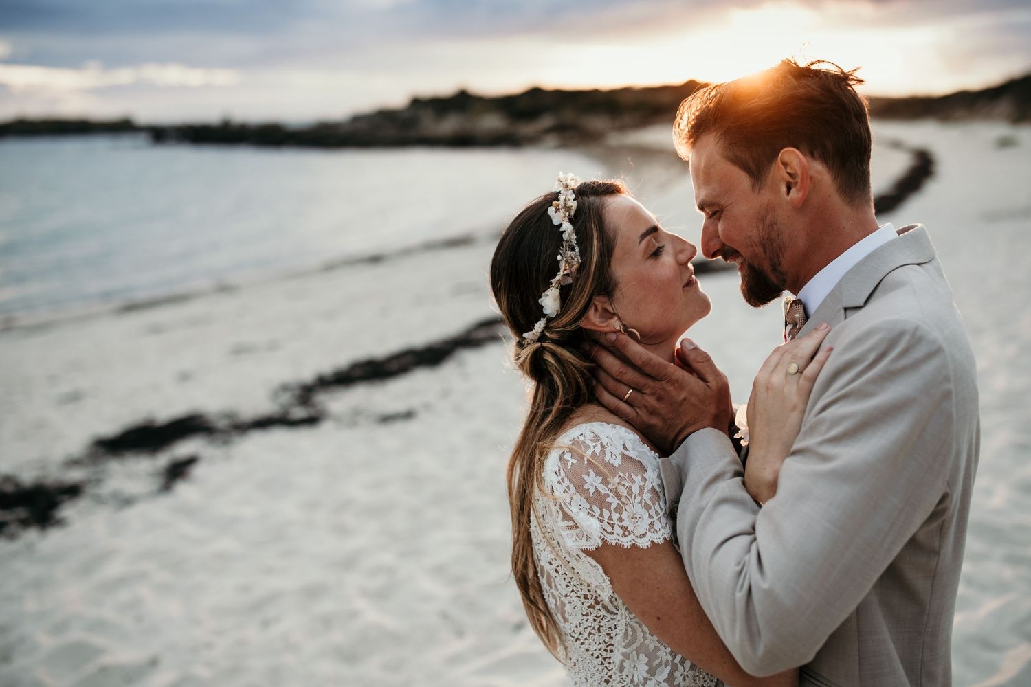 A romantic coastal wedding portrait with dramatic clouds and sunset lighting.