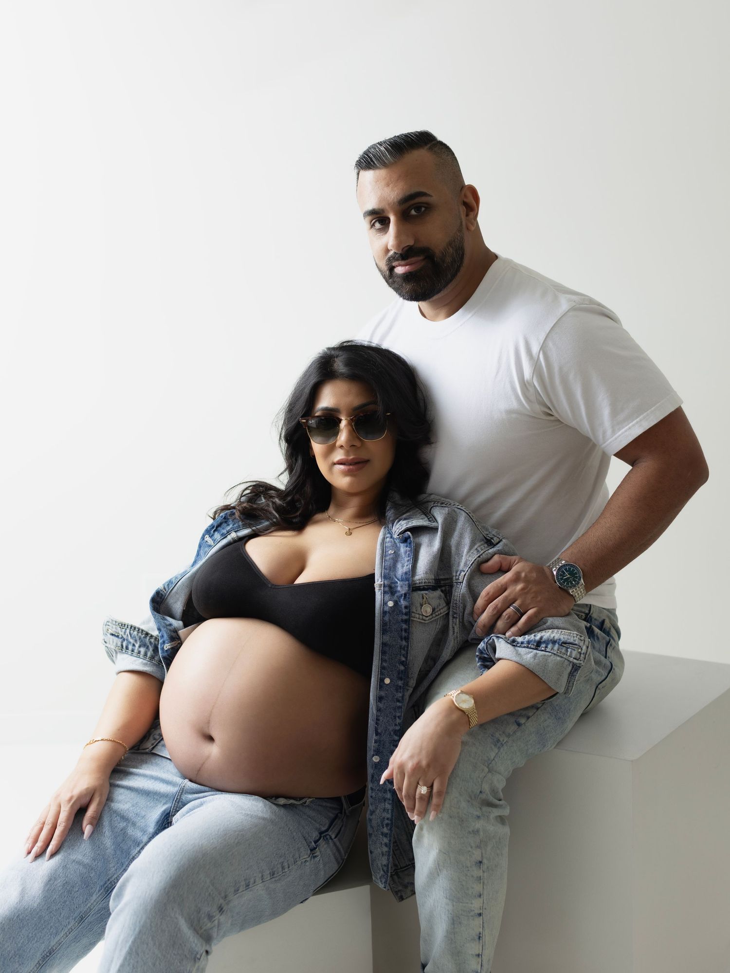 A series of maternity photos showing a couple in casual attire posing together against a white wall.