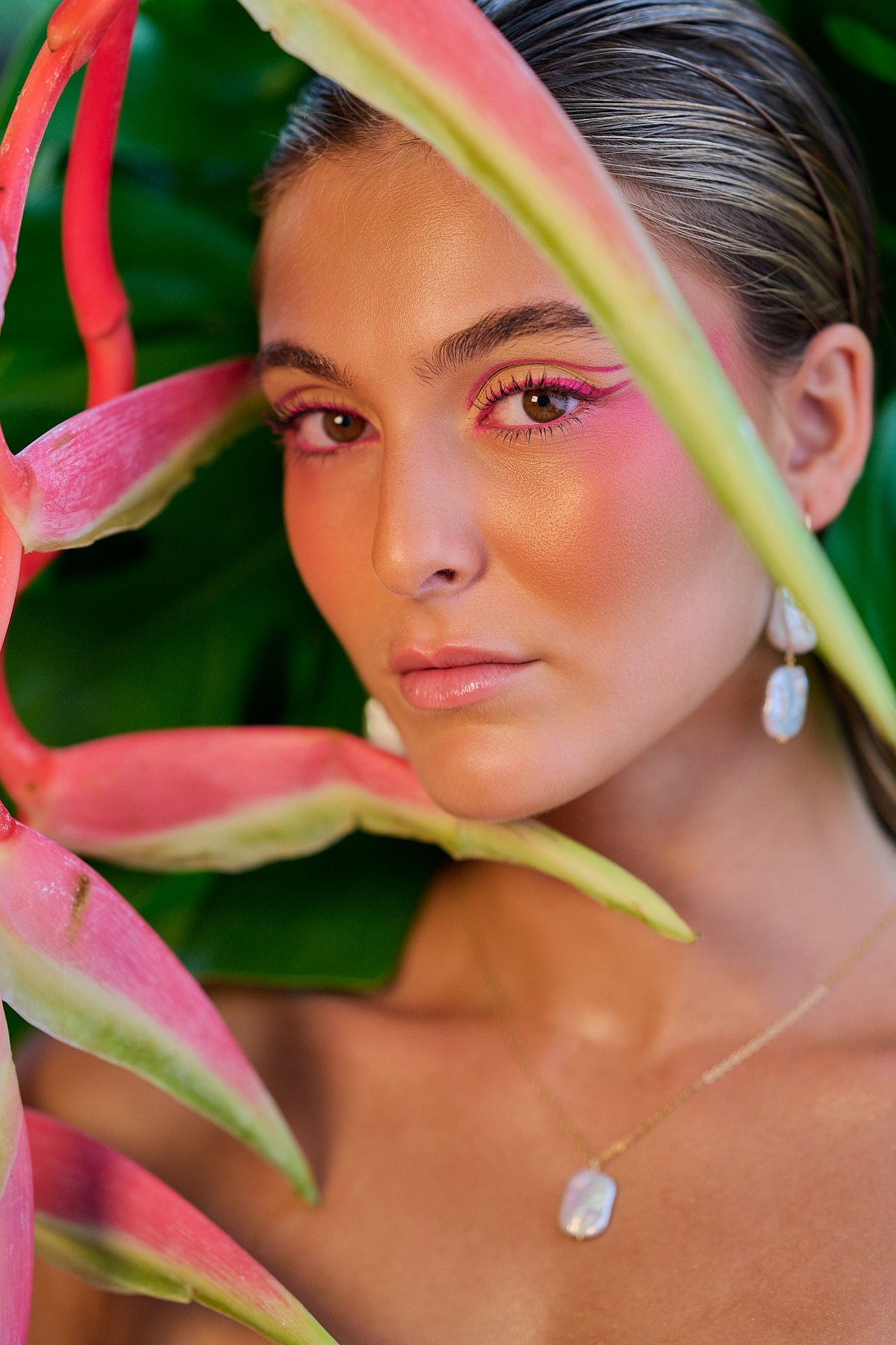 Artistic beauty portrait with pink heliconia flowers framing the composition against a green background.