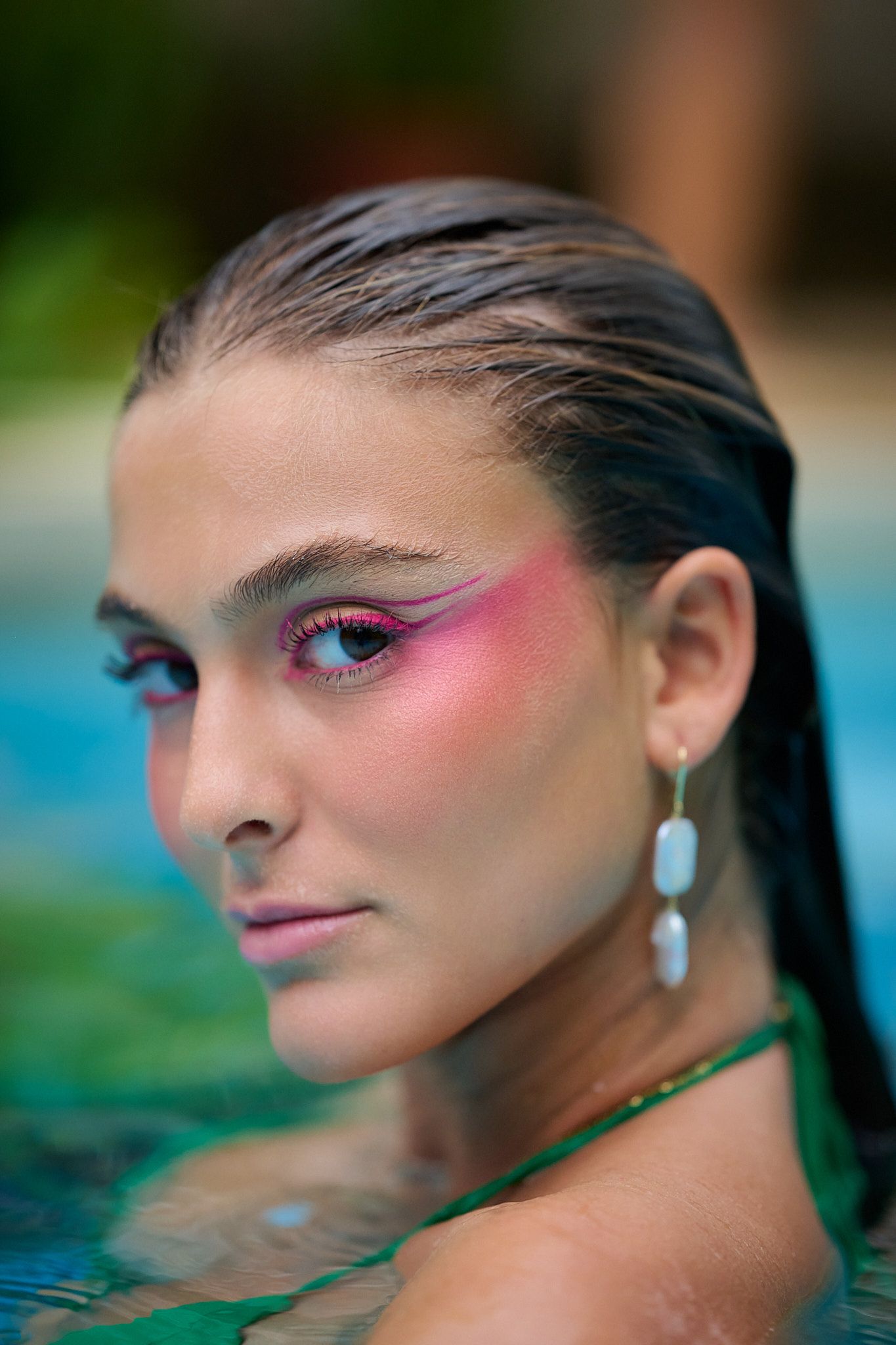 Close-up beauty shots showing vibrant pink makeup and teardrop earrings in an aquatic setting.