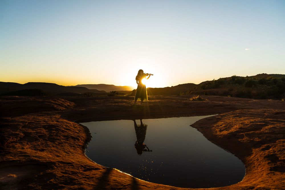 Dramatic sunset silhouettes against red rock formations and a reflective lake in a desert landscape.
